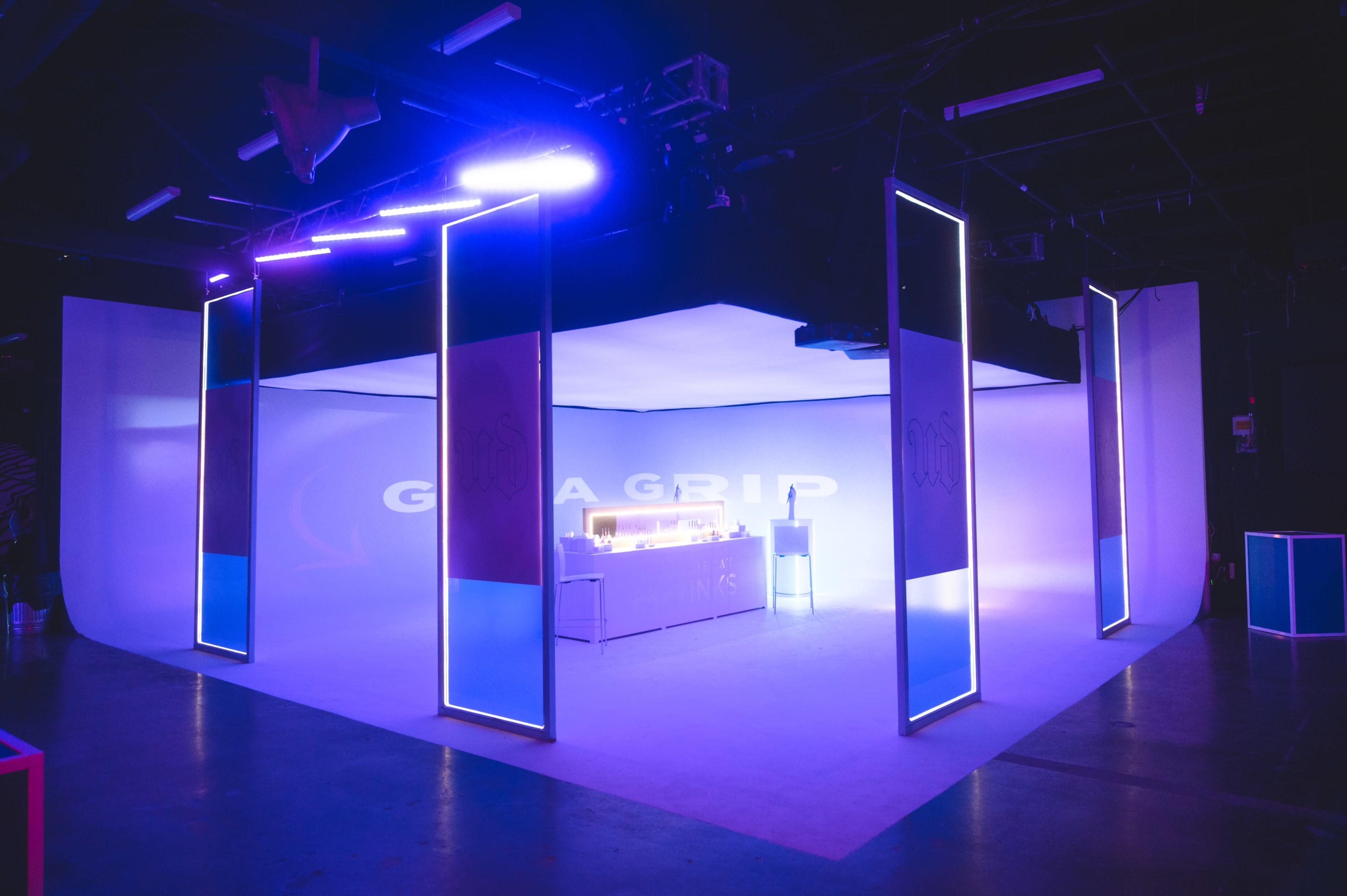 A brightly lit exhibition space features a minimalistic setup with glowing panels and a central display counter.