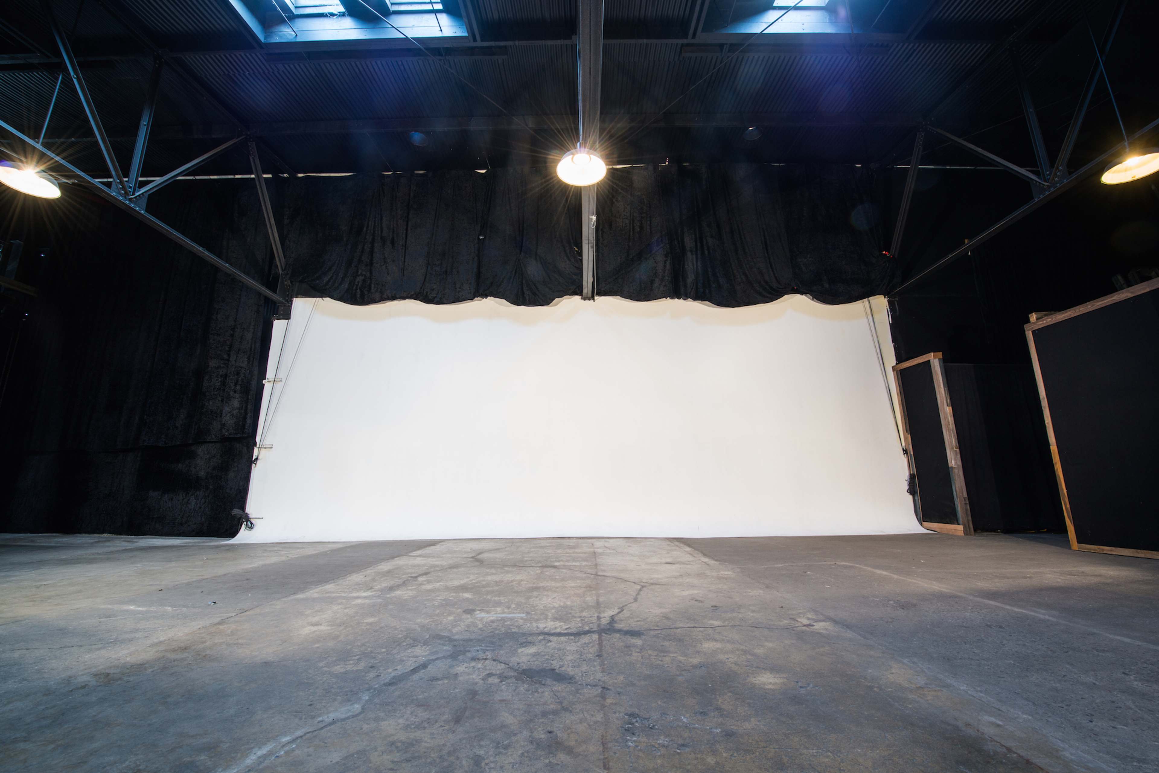 An empty industrial space features a large white backdrop and black curtains against a concrete floor.