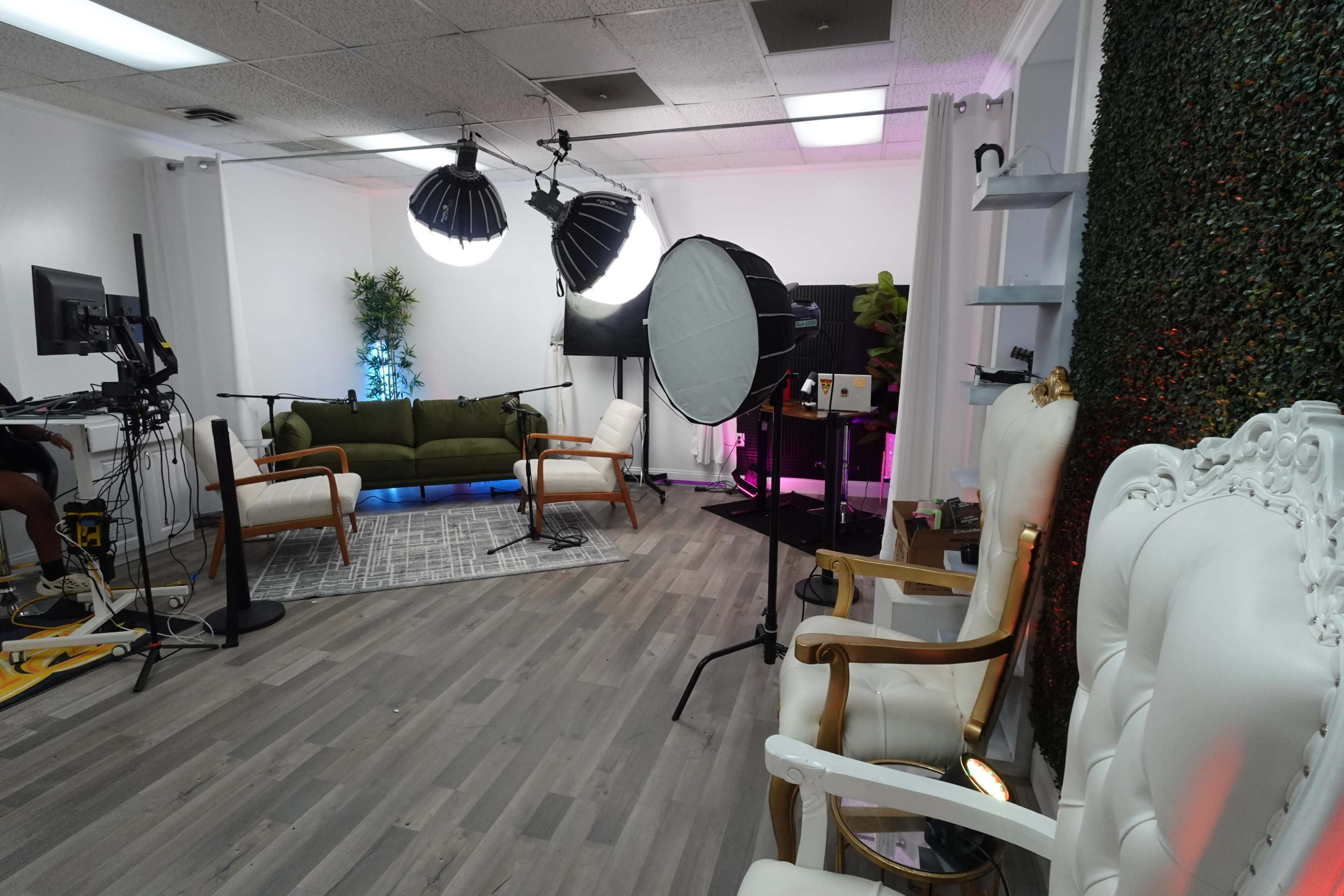 A modern studio setup with green sofas, microphones, and lighting equipment arranged for a recording session.