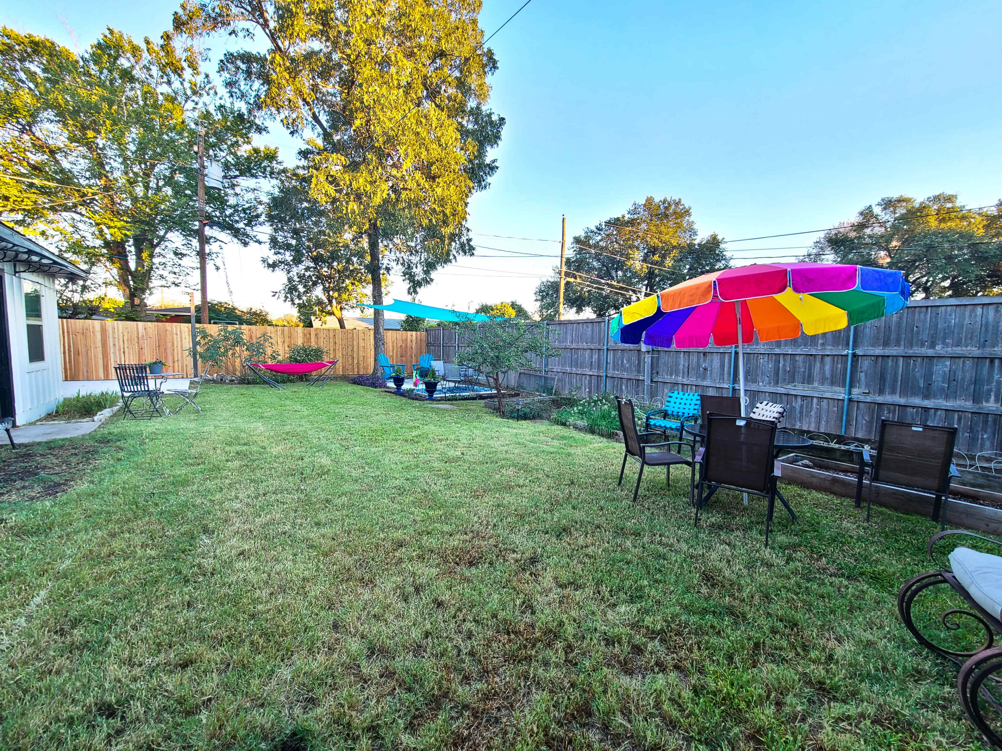 A grassy backyard with seating areas, colorful umbrellas, and trees in the background.