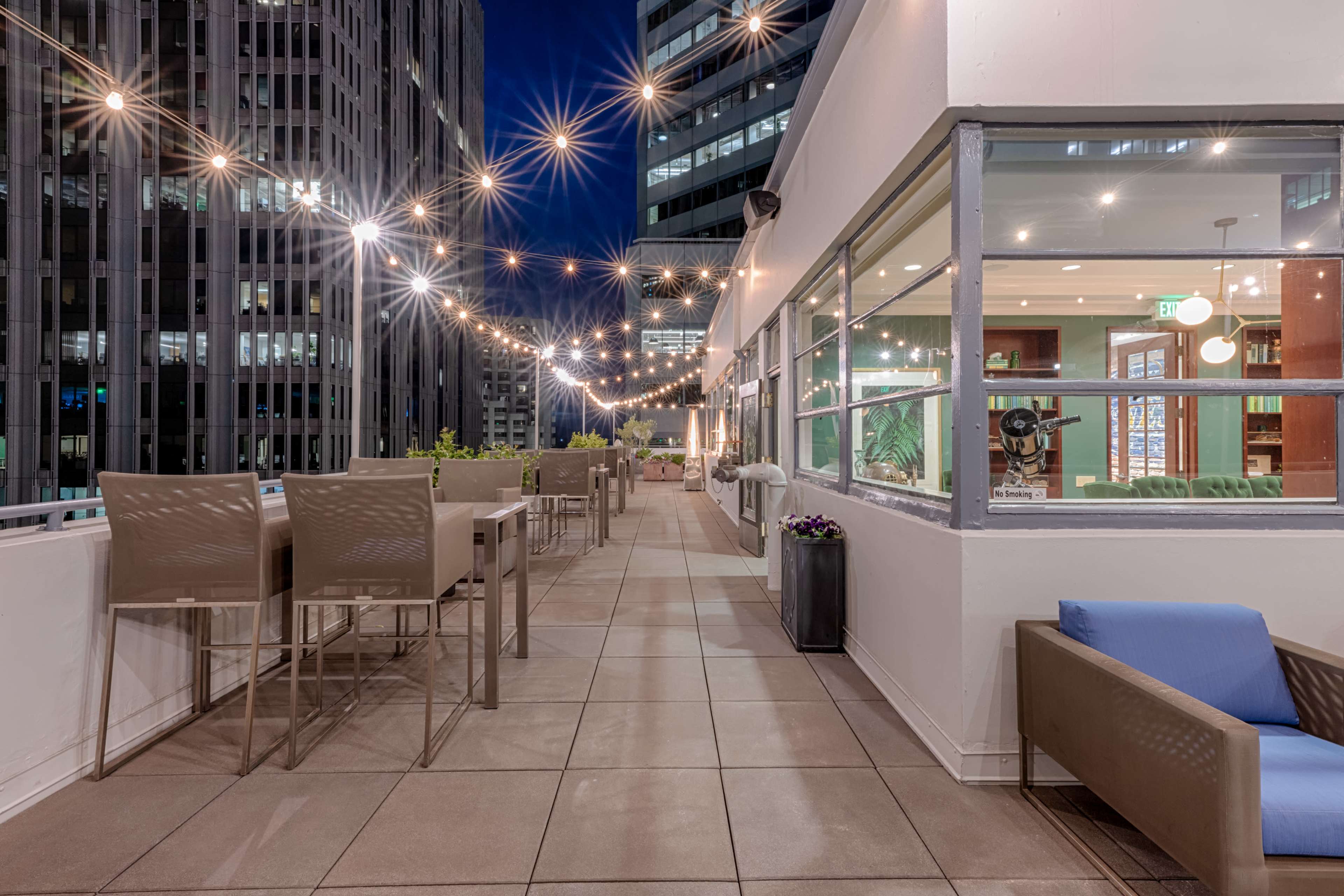 A rooftop terrace with string lights, offering a view of surrounding buildings at night.