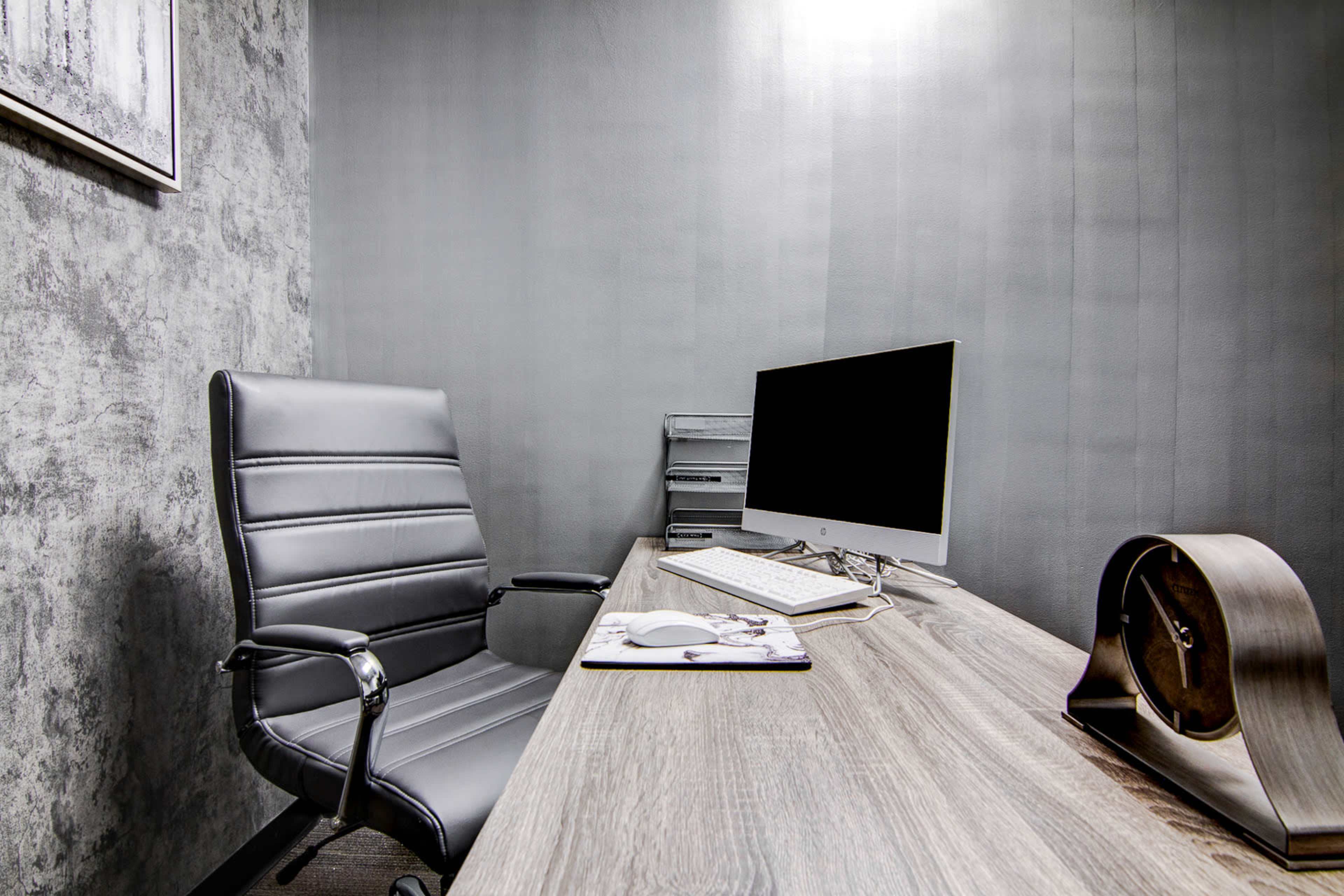 A minimalist office space with a black ergonomic chair, a wooden desk, a computer monitor, and a clock.
