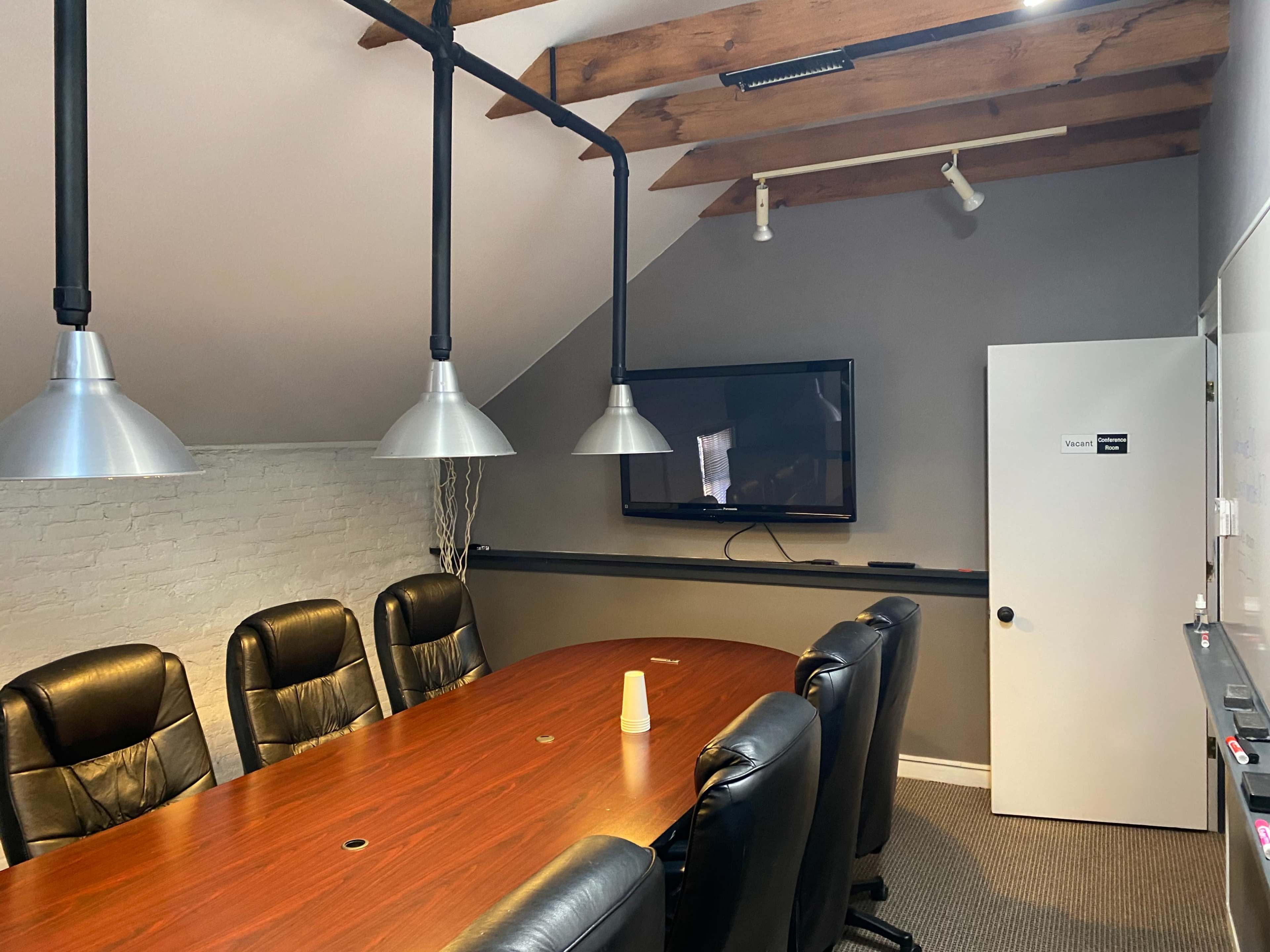 The image shows a conference room with a long wooden table surrounded by black leather chairs, a wall-mounted television, and a door labeled "Toilet."