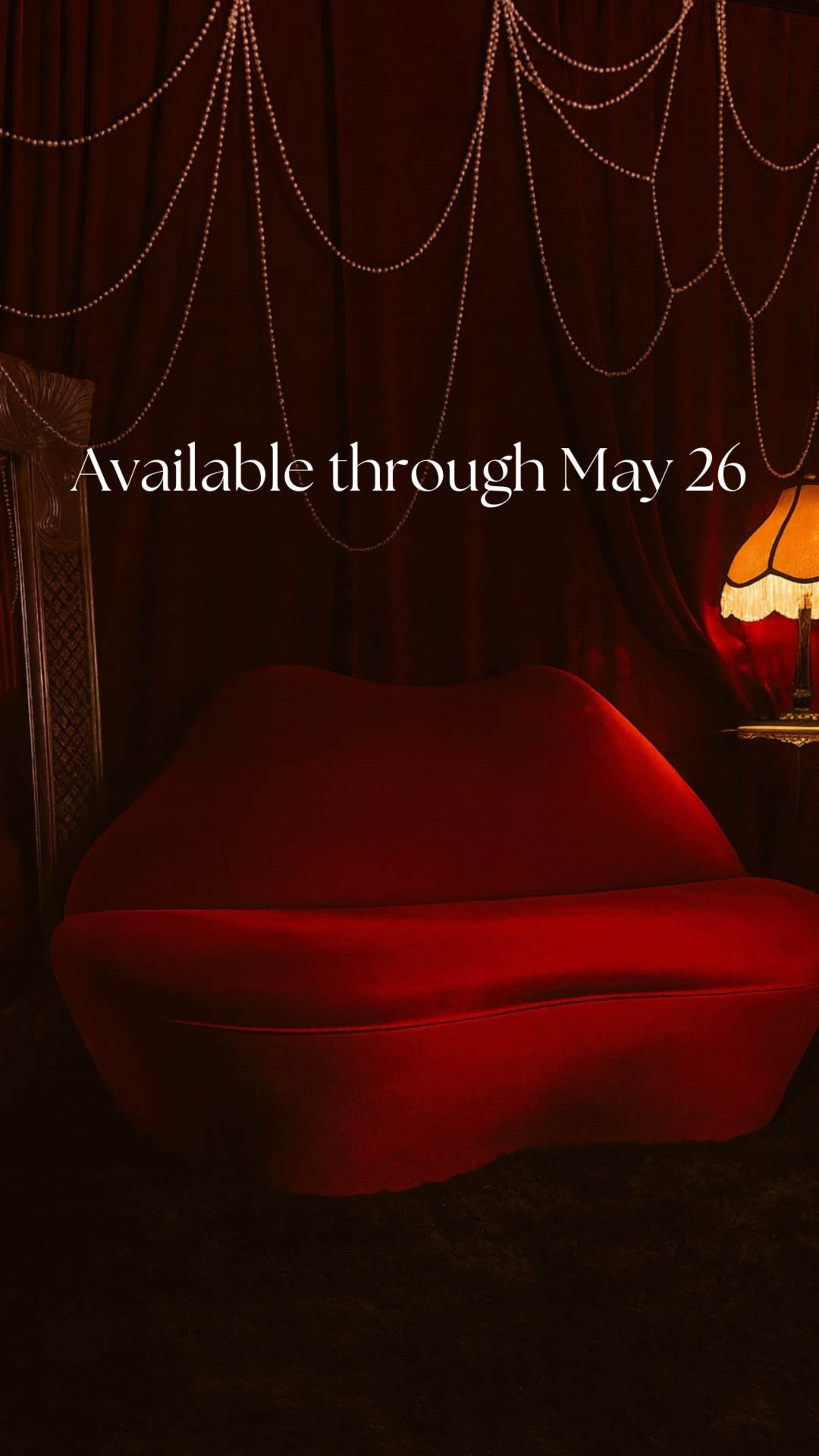 A red sofa sits against a dark backdrop with decorative string lights and a lamp beside it.