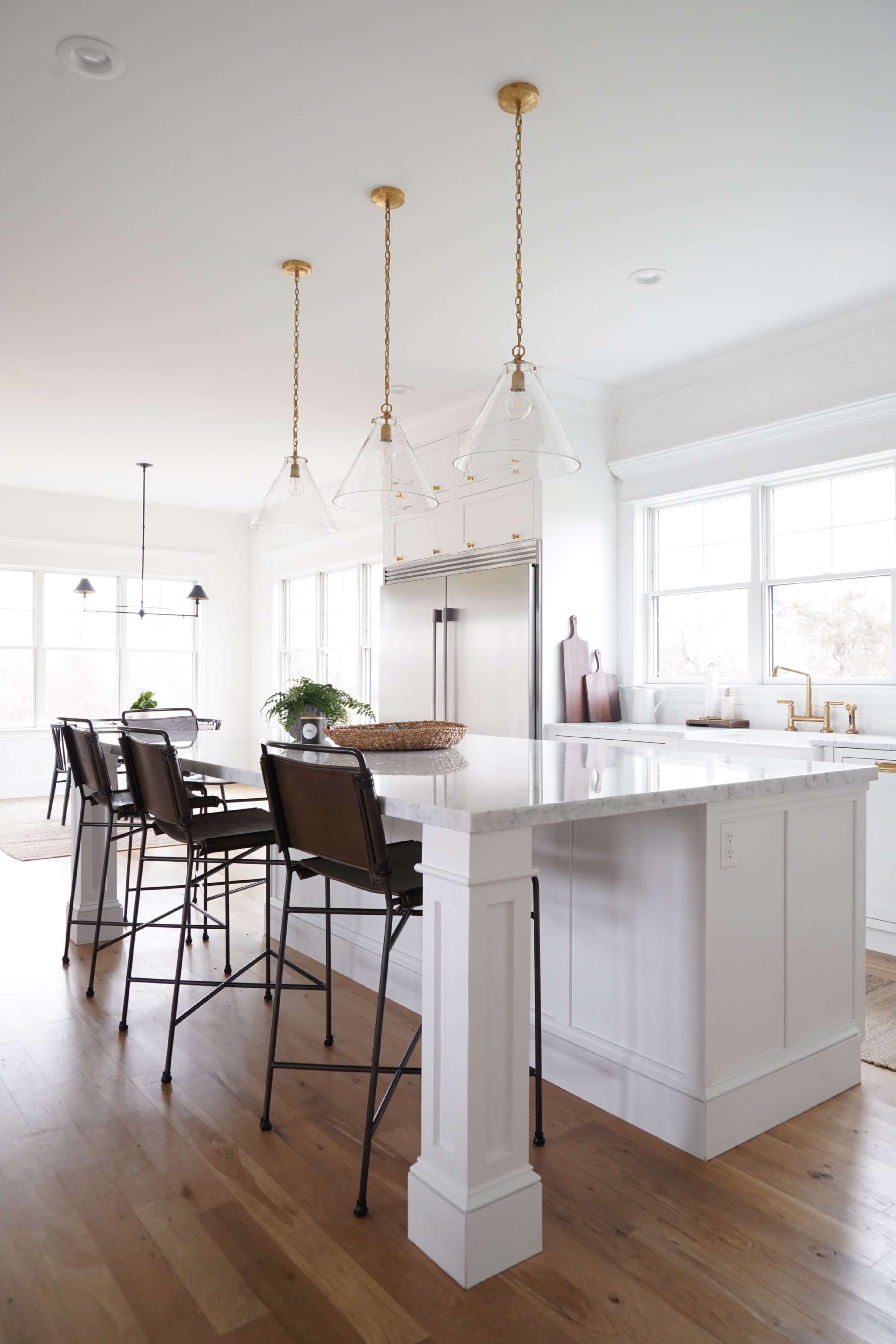 A modern kitchen features a white island with bar stools, gold pendant lights, and stainless steel appliances.