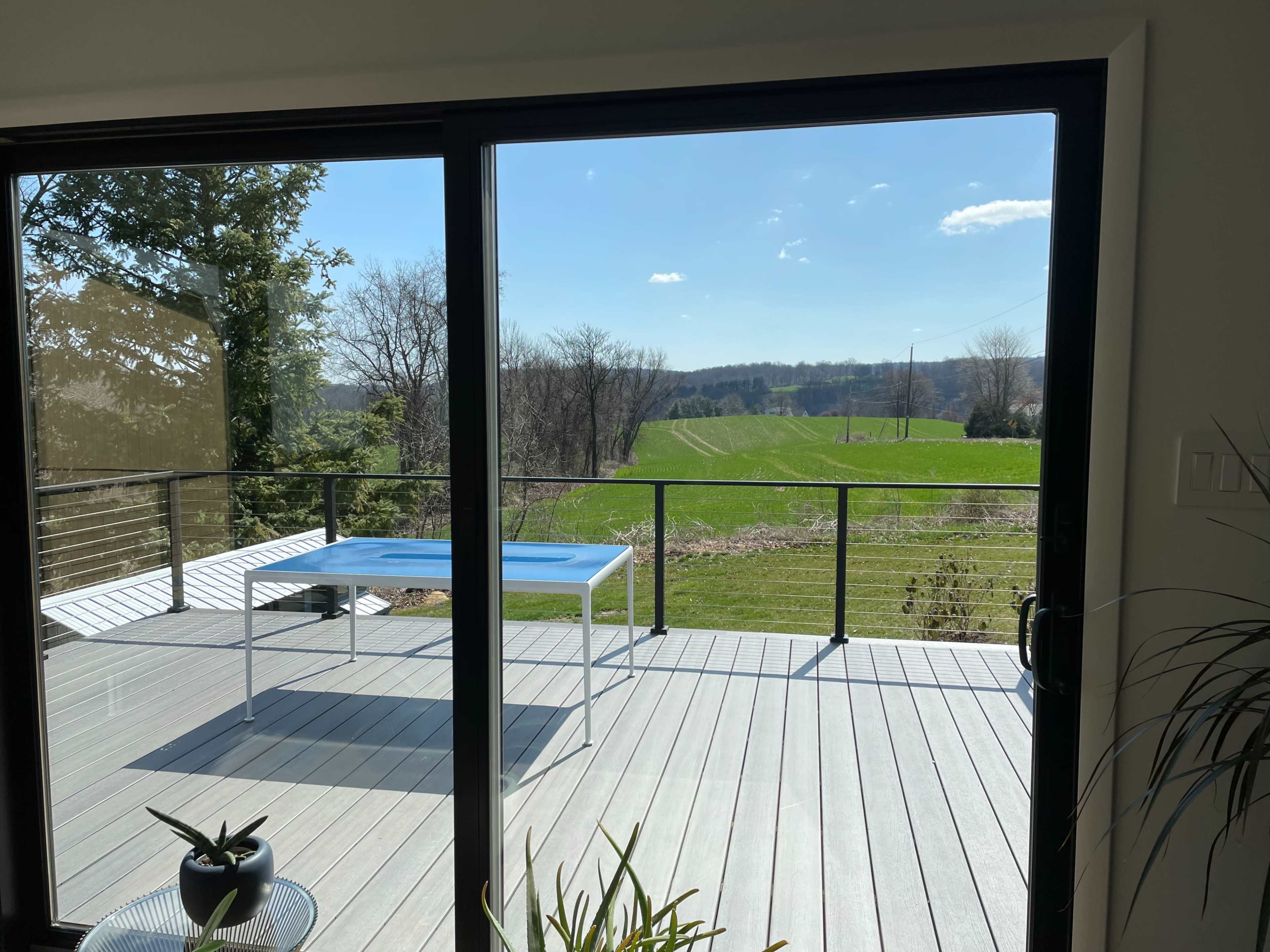 A clear view of a green field is visible through a glass door, framed by a wooden deck and a simple table.