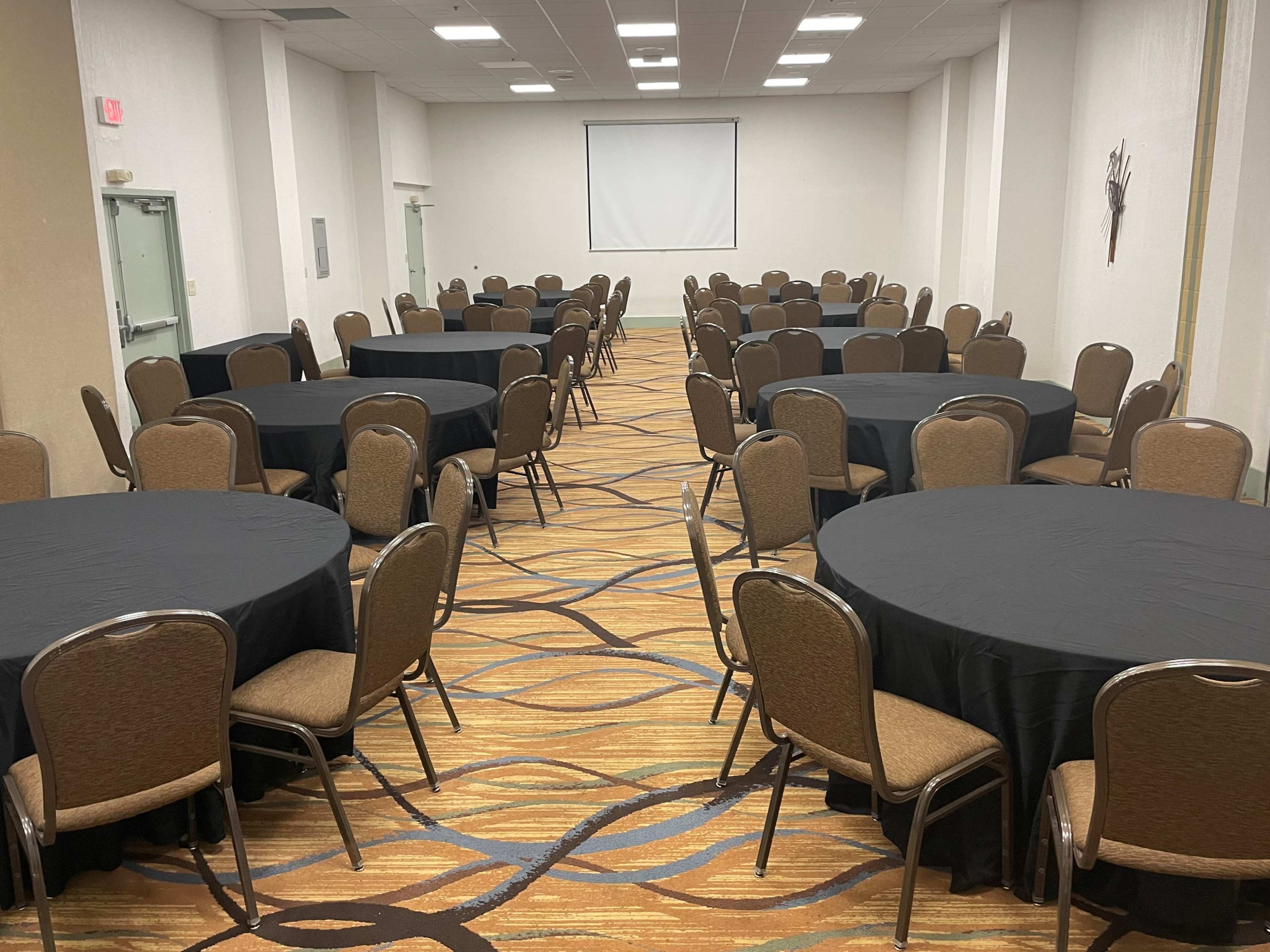 A large room is set up with multiple tables covered in black tablecloths arranged in rows.