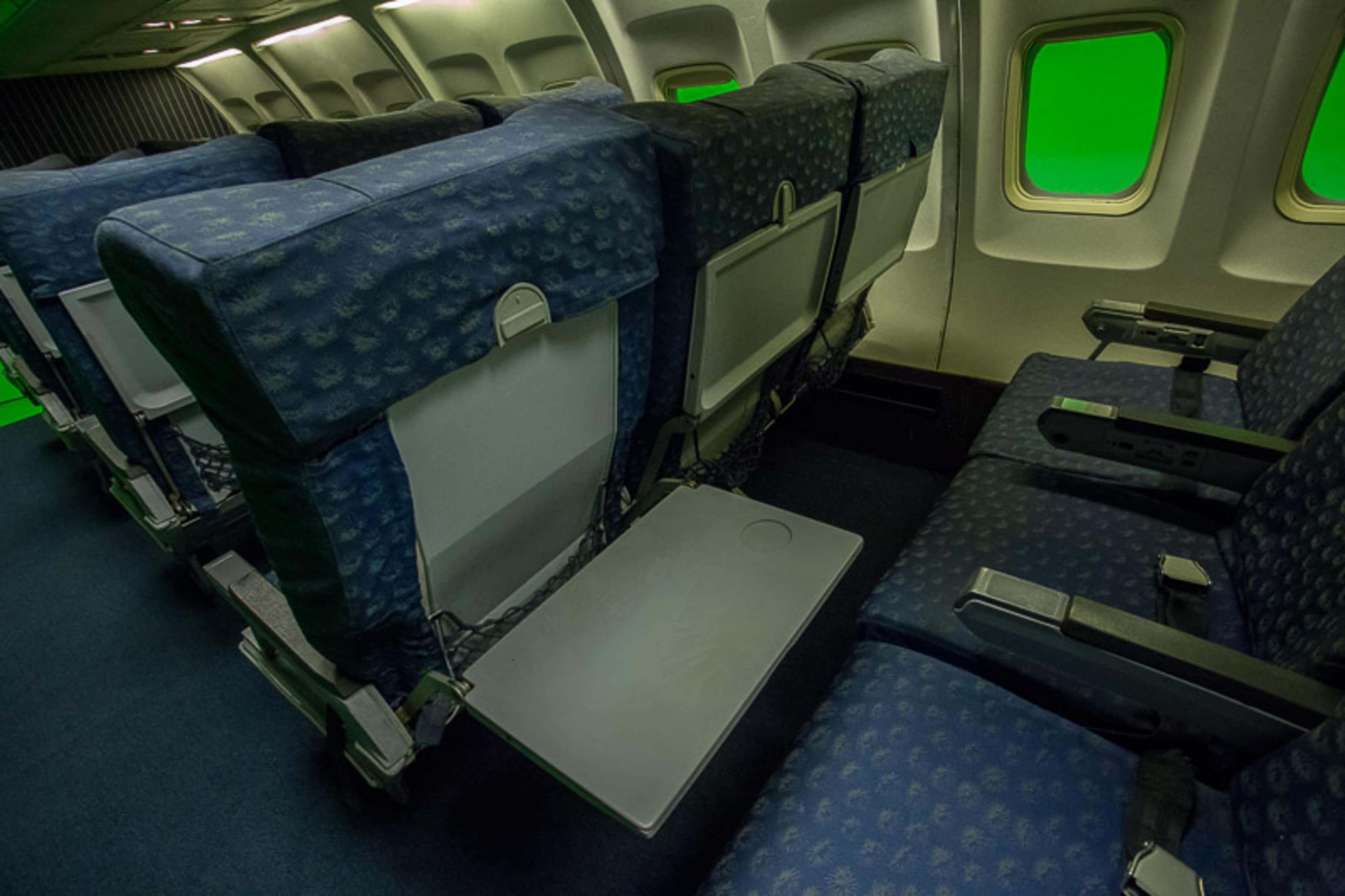 A row of airplane seats with blue upholstery and a fold-down tray table in a cabin interior.