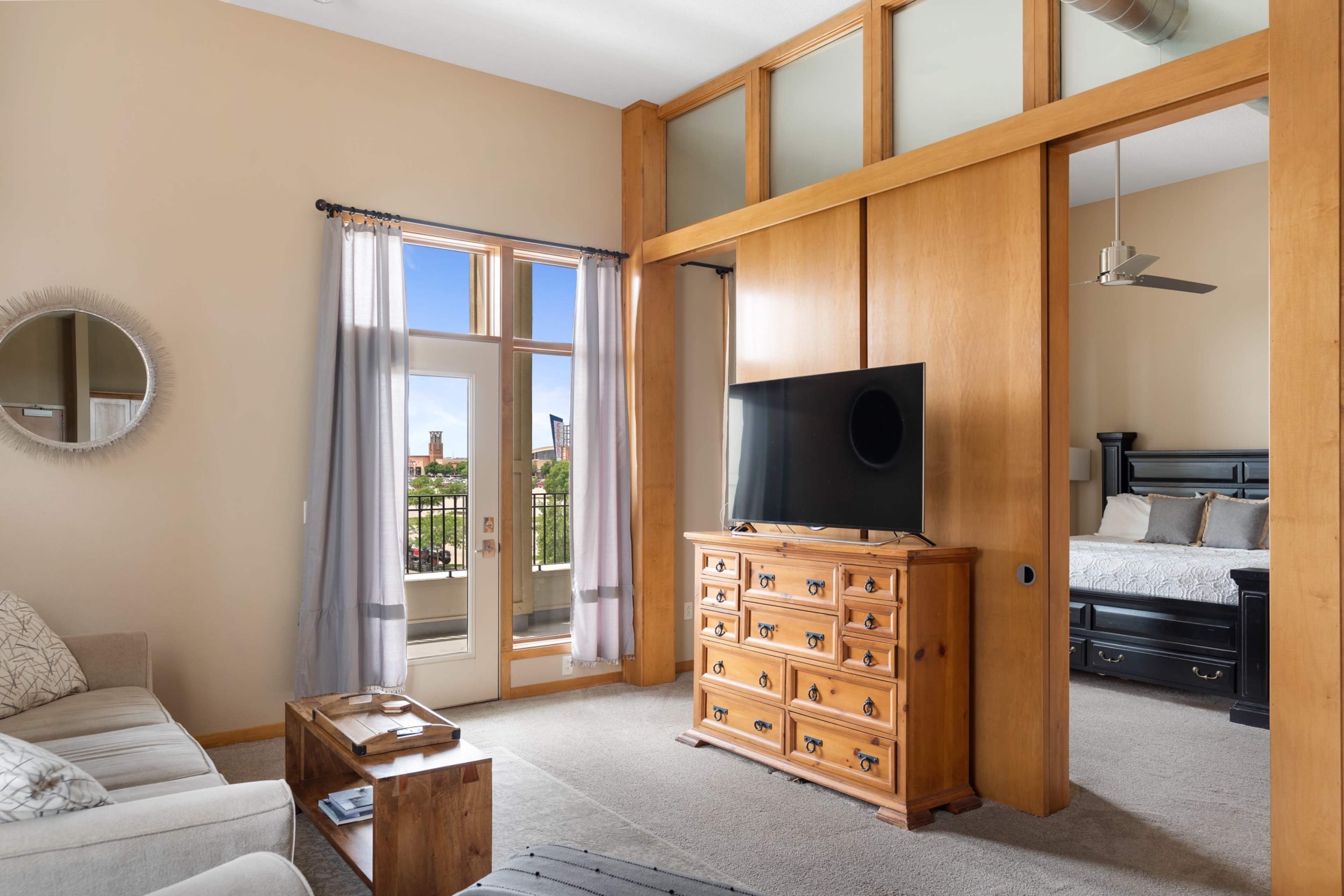 A modern living space with a comfortable seating area, a wooden dresser, and a television, separated from a bedroom by a wooden partition.