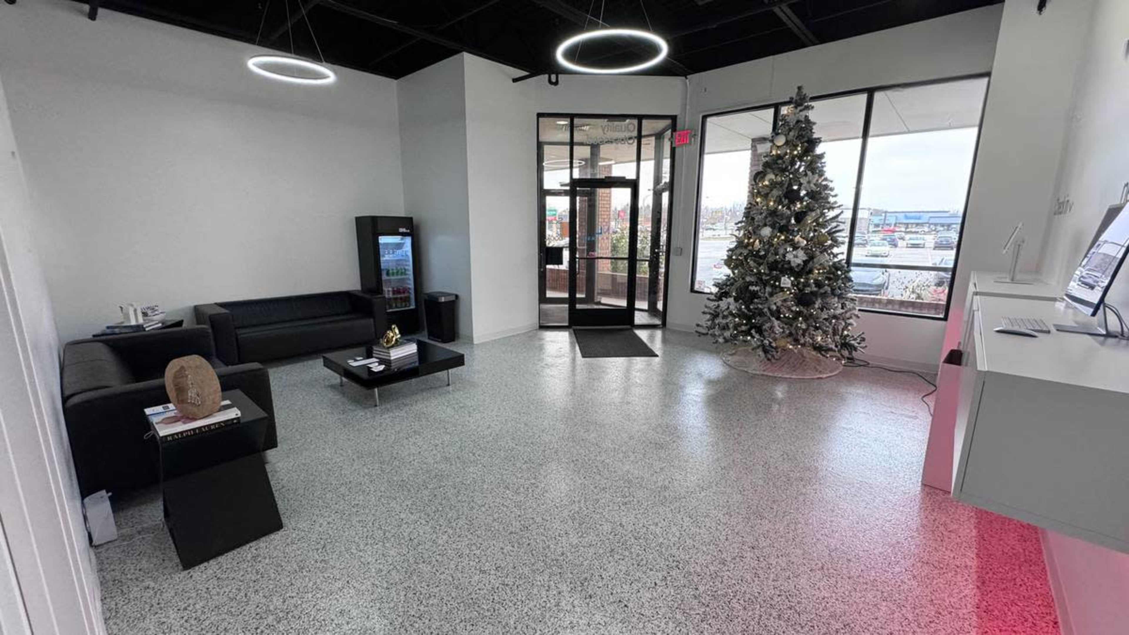 A modern, spacious lobby featuring a Christmas tree, a seating area with black couches, and a glass entrance.