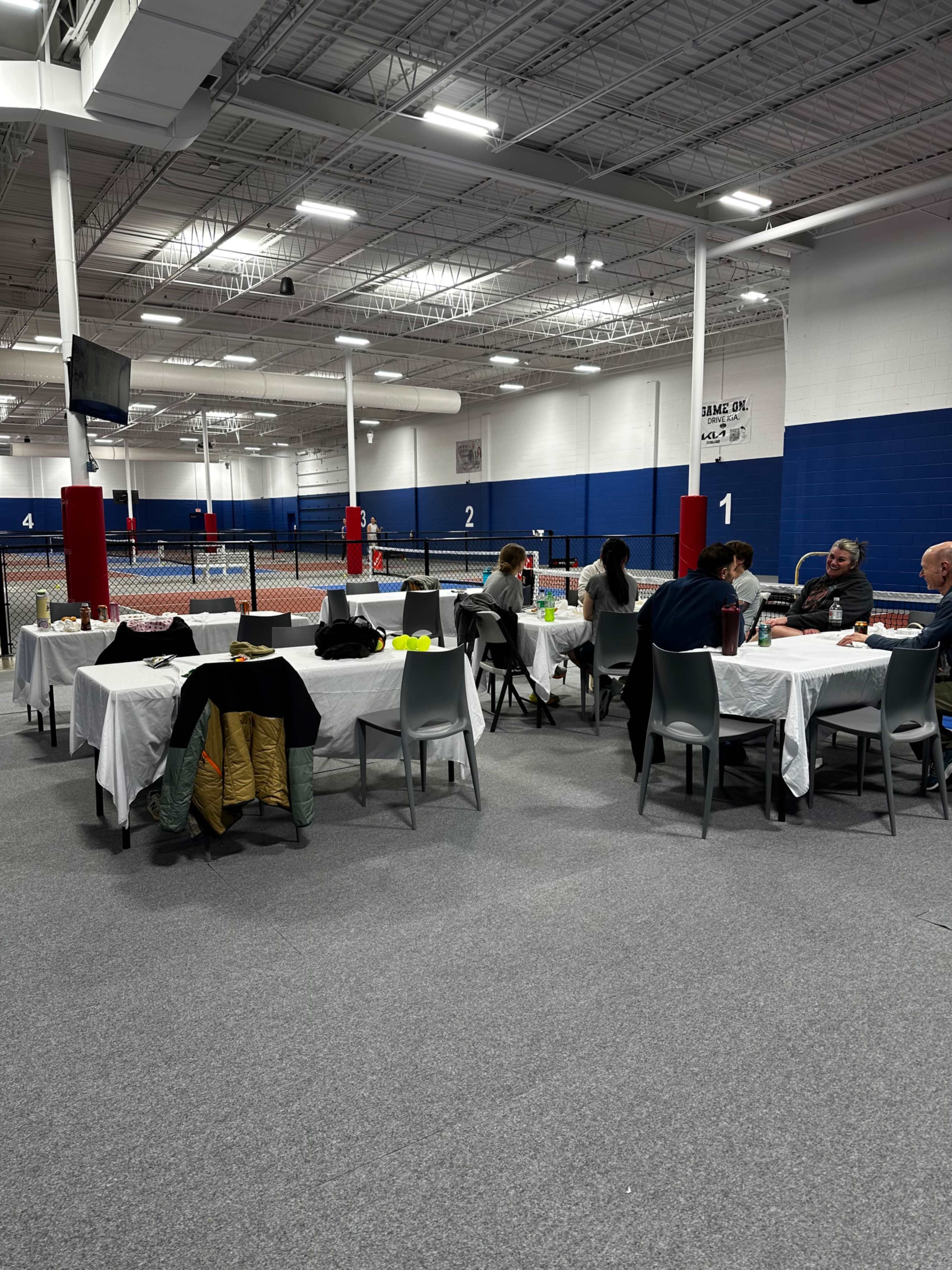 The image shows a spacious indoor venue with several tables set for dining, where people are seated and enjoying a meal.