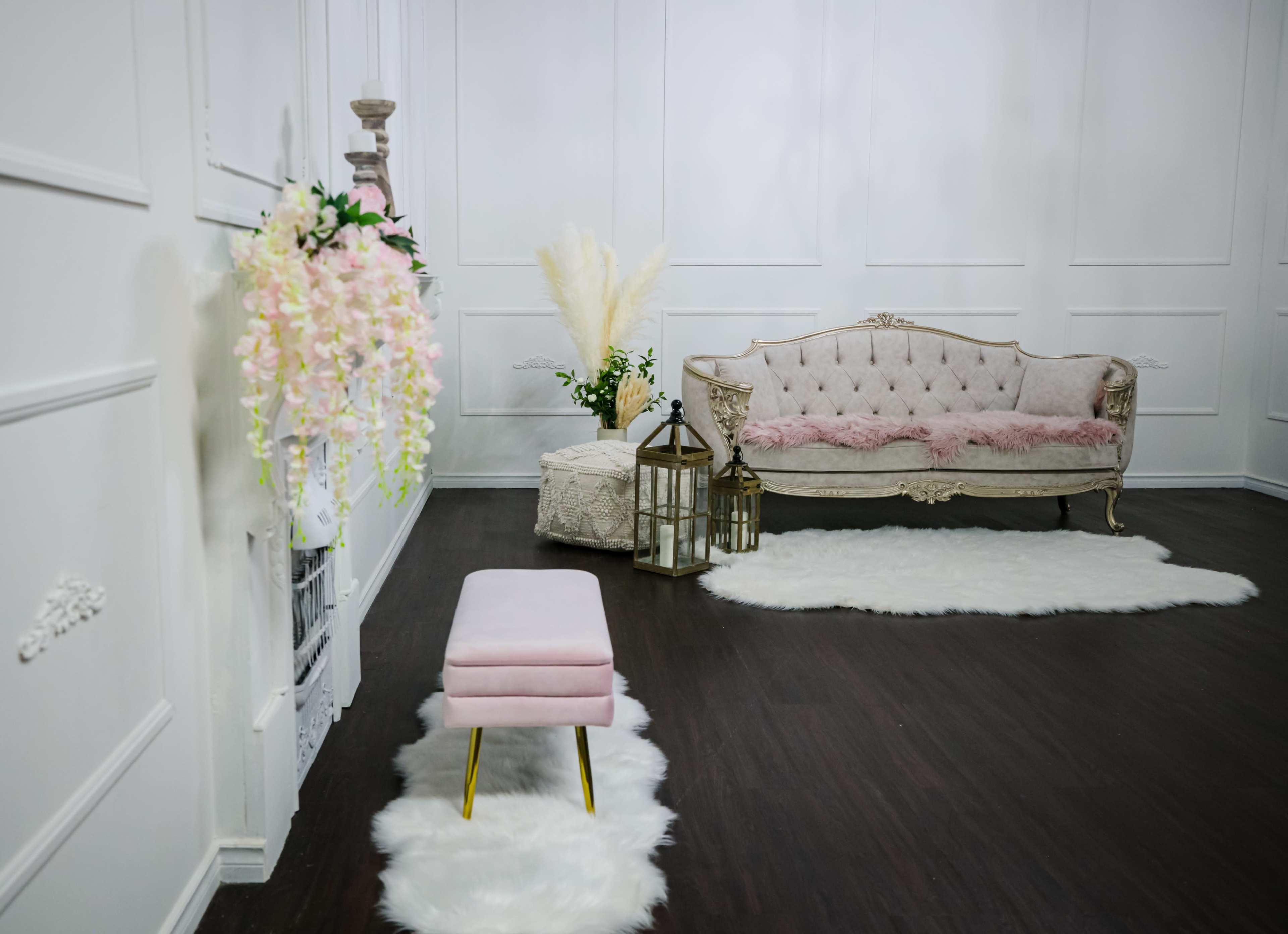 A decorated room with a pink sofa, a matching stool, and a white fluffy rug on a dark wooden floor.