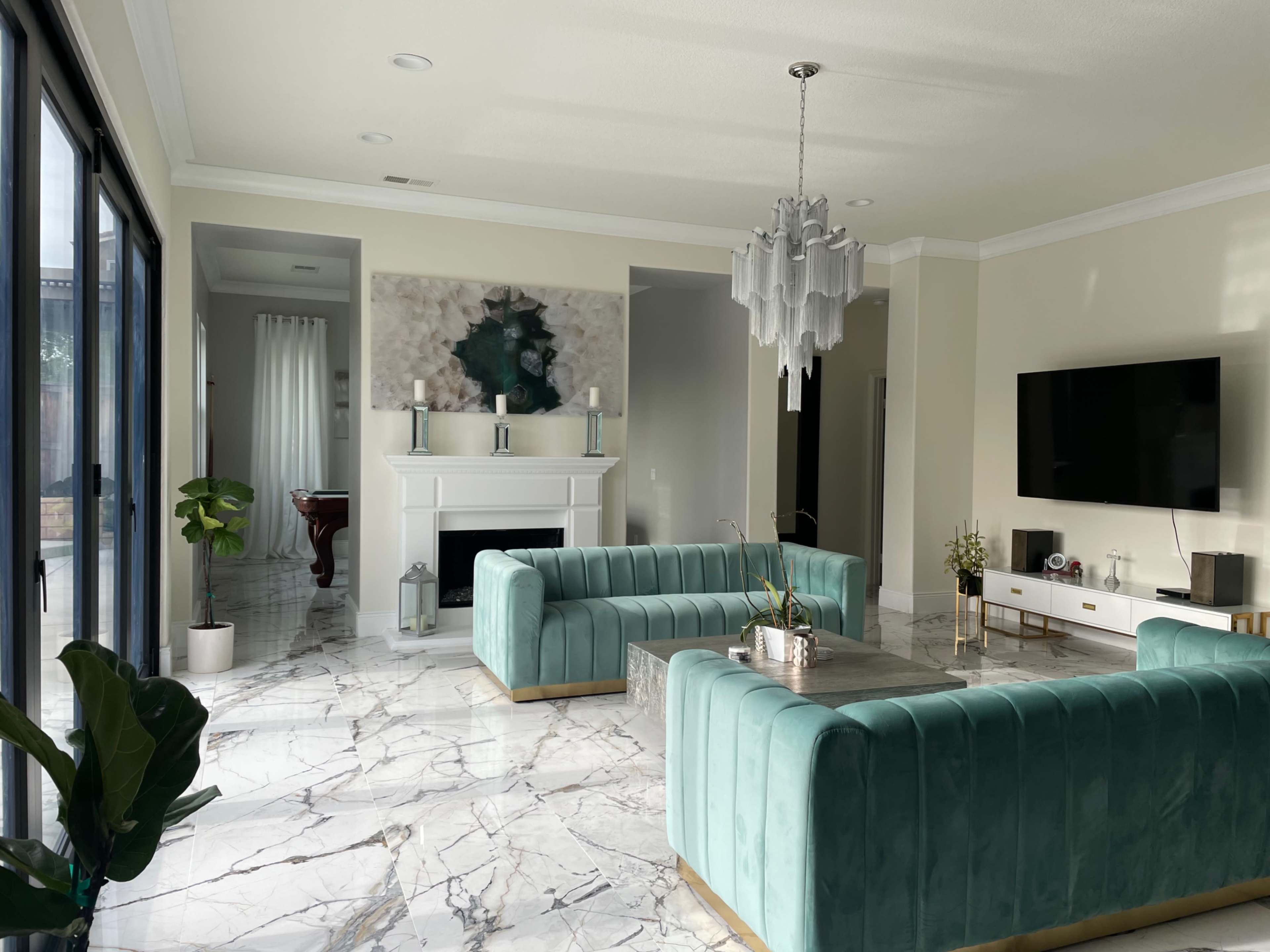 A modern living room featuring two light blue velvet sofas facing a coffee table, with a fireplace, large windows, and contemporary decor.