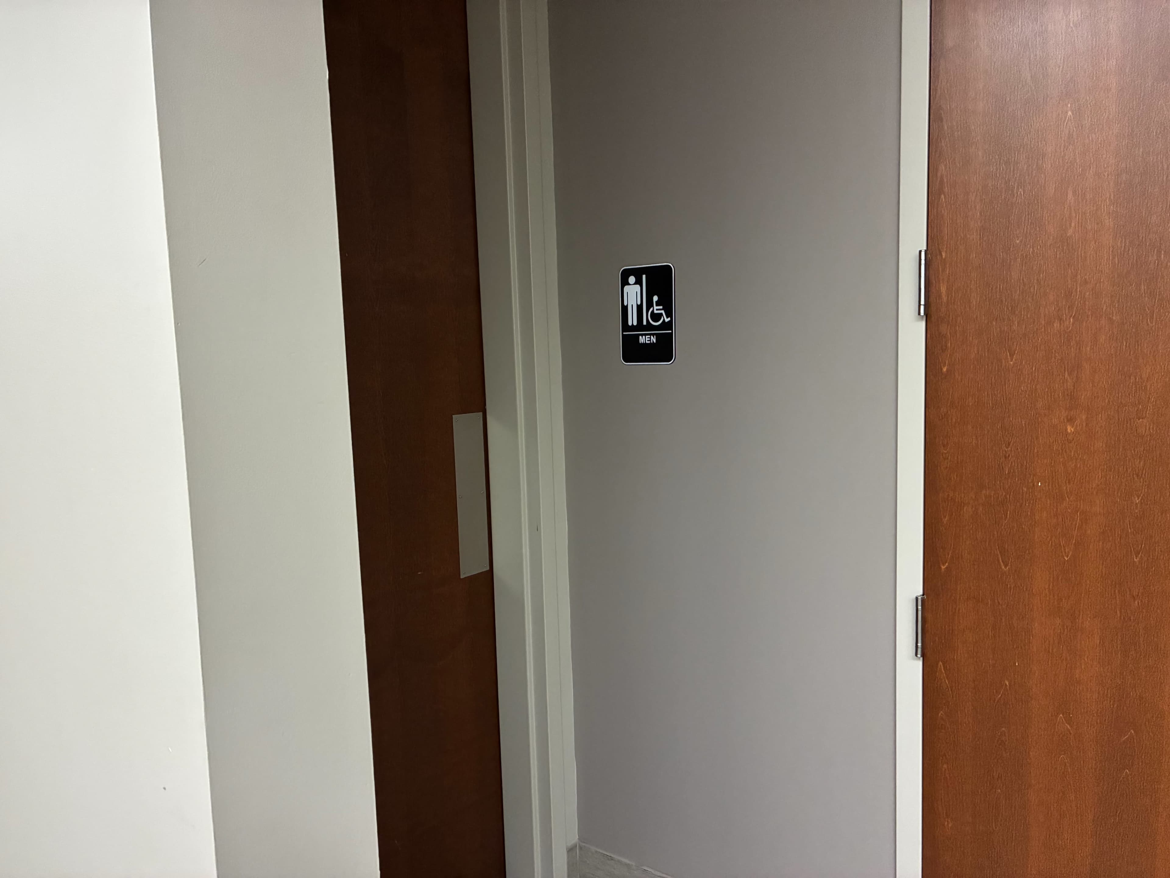 The image shows a restroom door with a sign indicating it is designated for both men and accessible for individuals with disabilities.