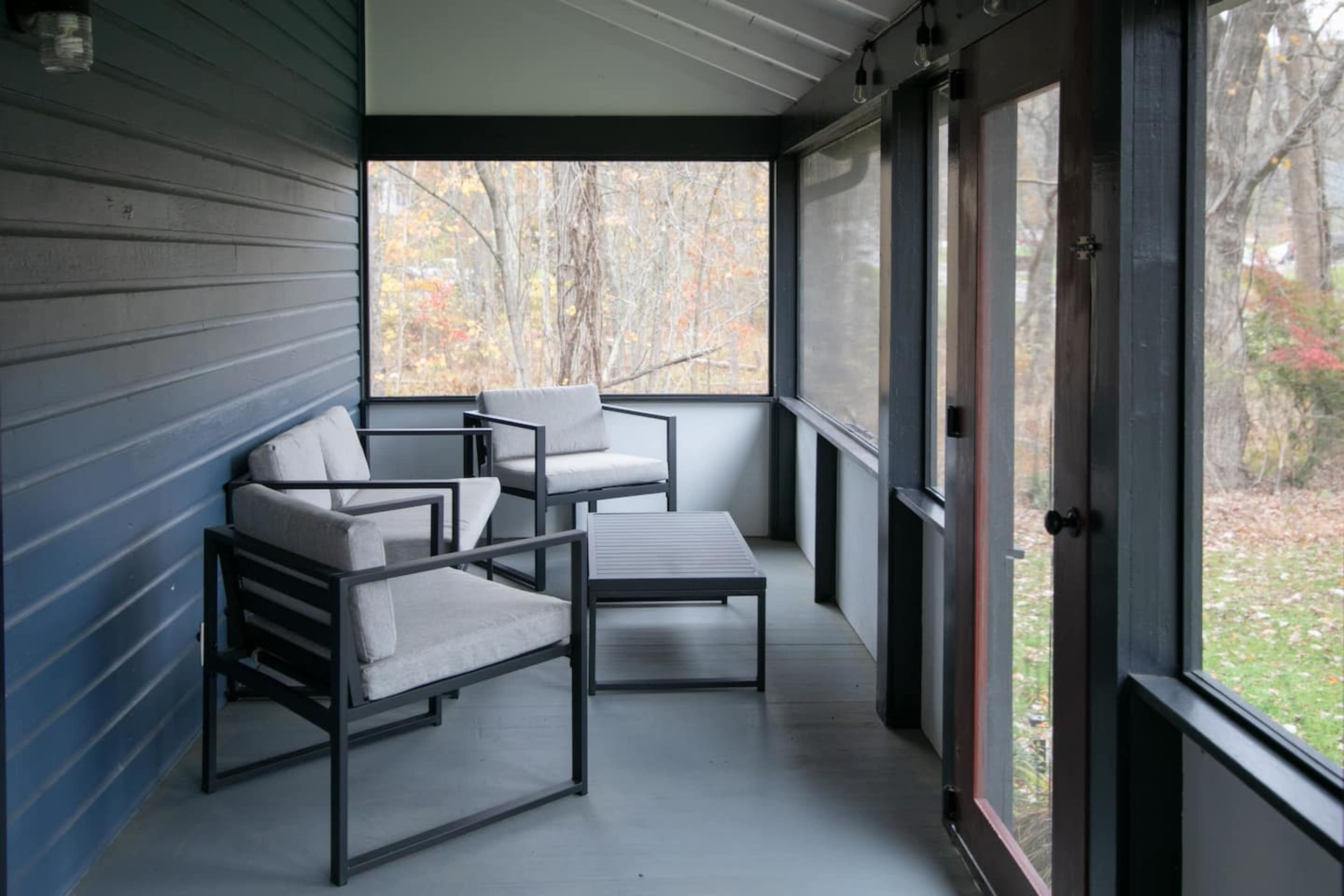 A screened-in porch featuring two gray chairs and a small table on a wooden floor.