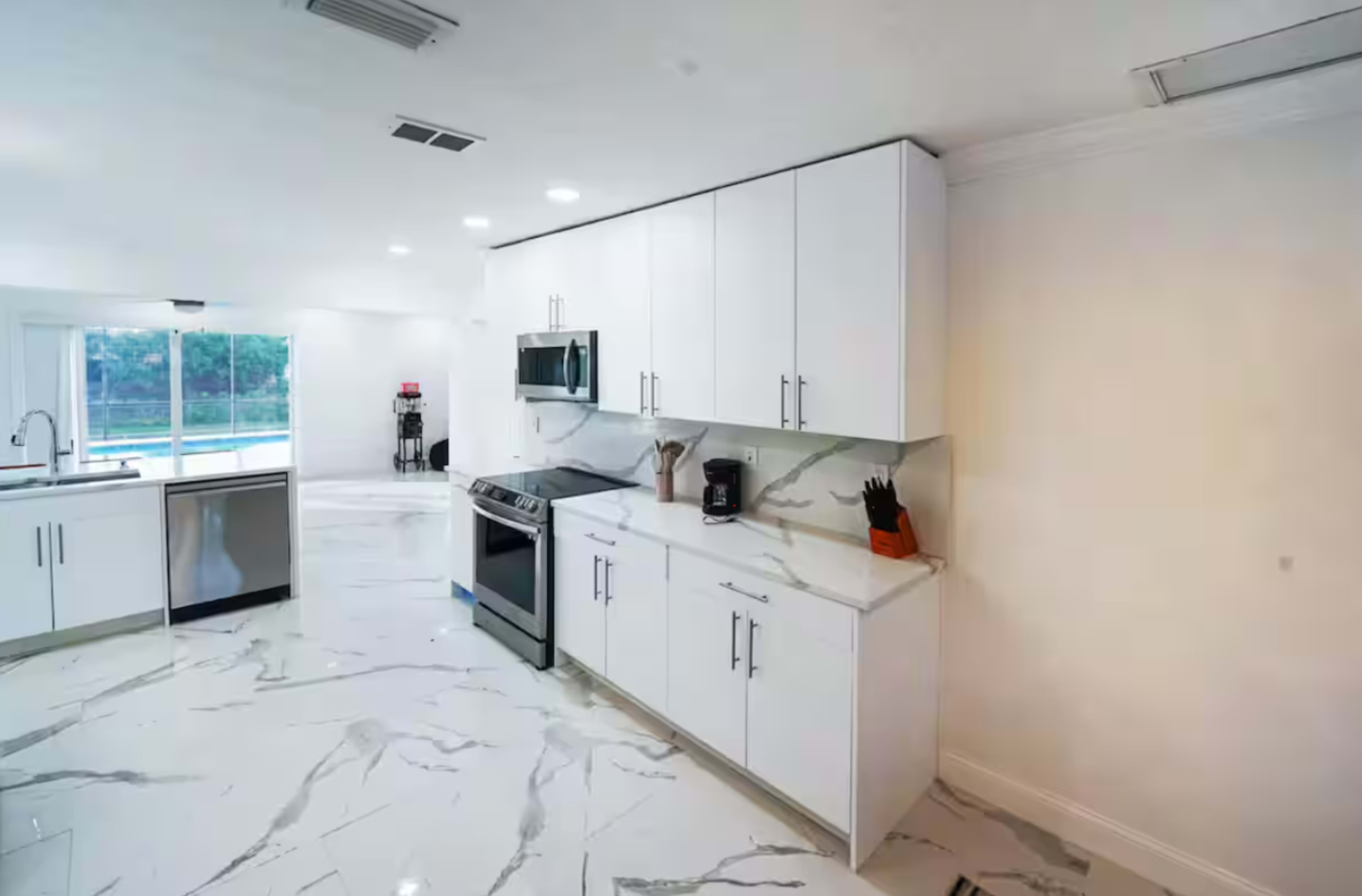 The image shows a modern kitchen with white cabinetry, stainless steel appliances, and a marble floor.