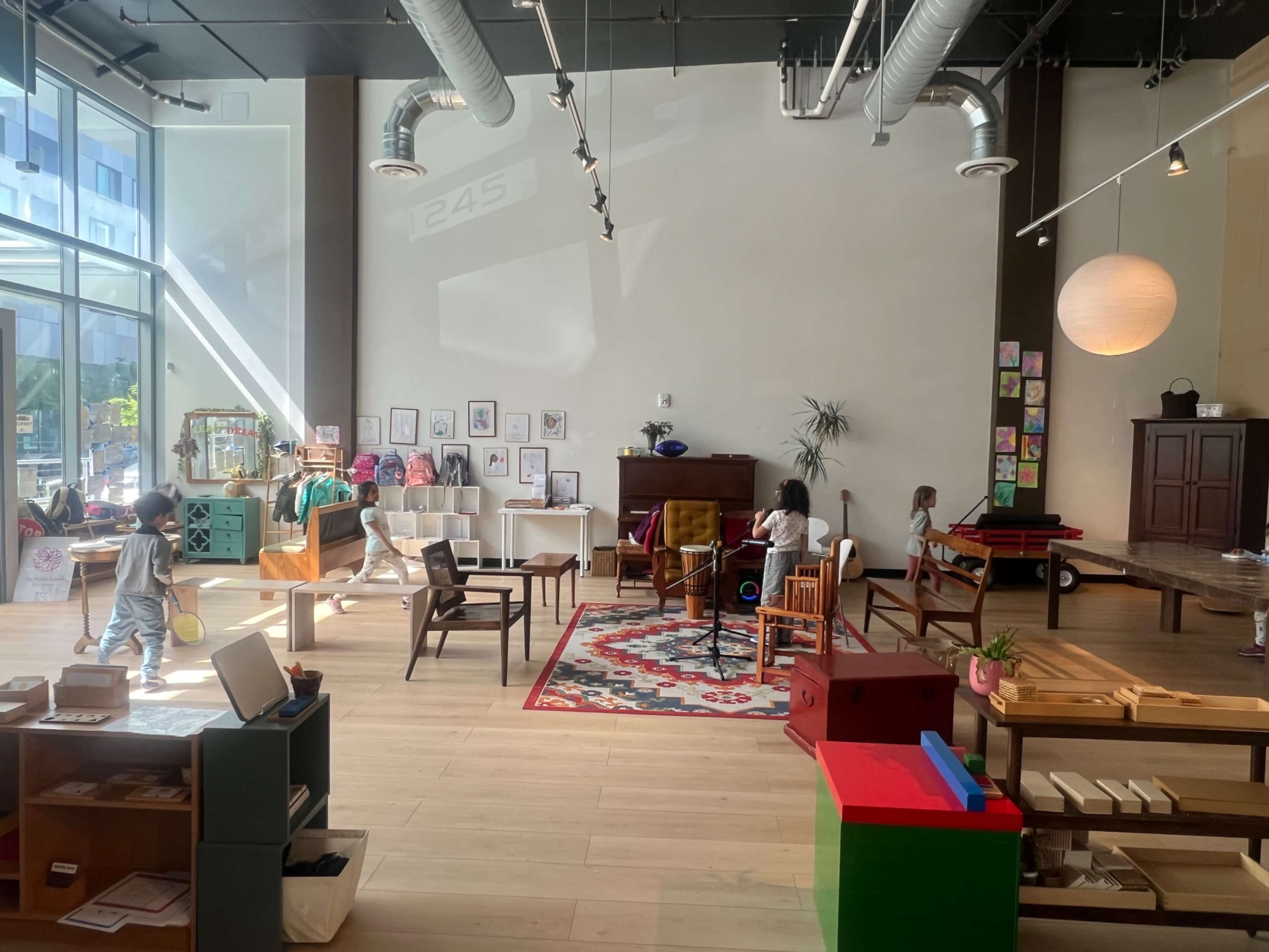 The image shows a spacious indoor play area with various furniture pieces, colorful toys, and children engaging in activities.