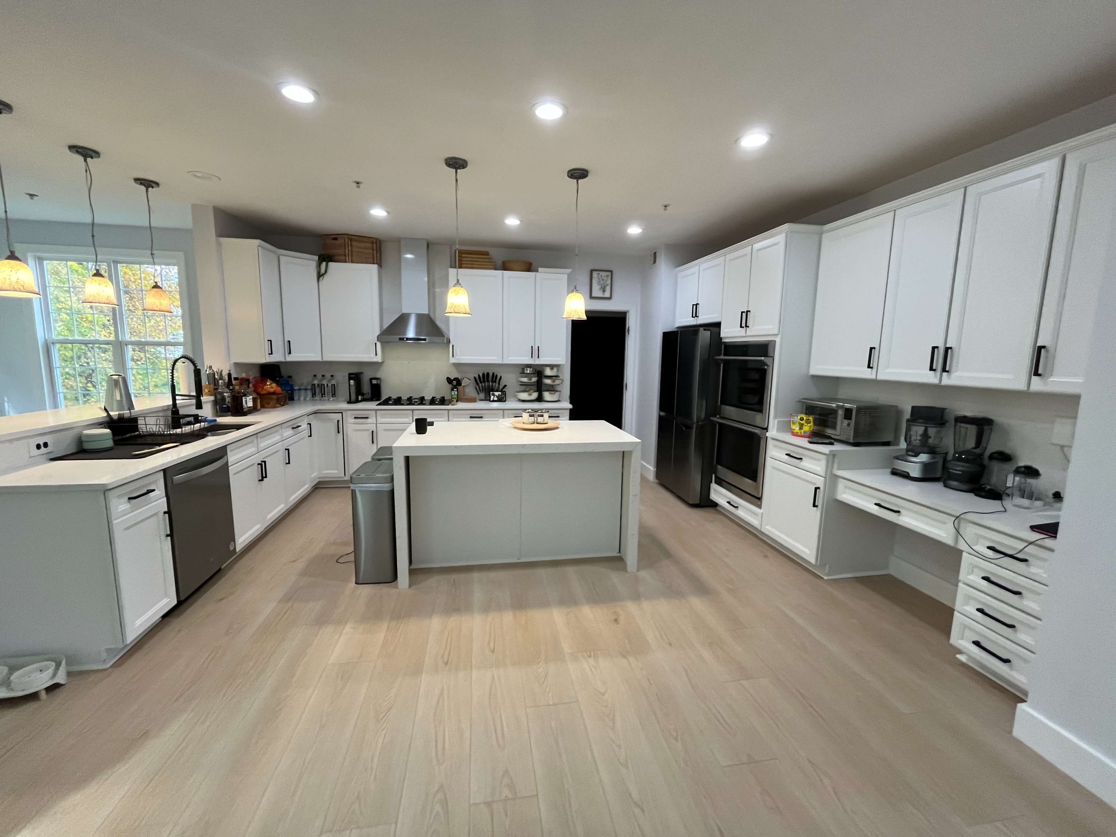 A modern kitchen features white cabinetry, stainless steel appliances, and a central island with pendant lighting.