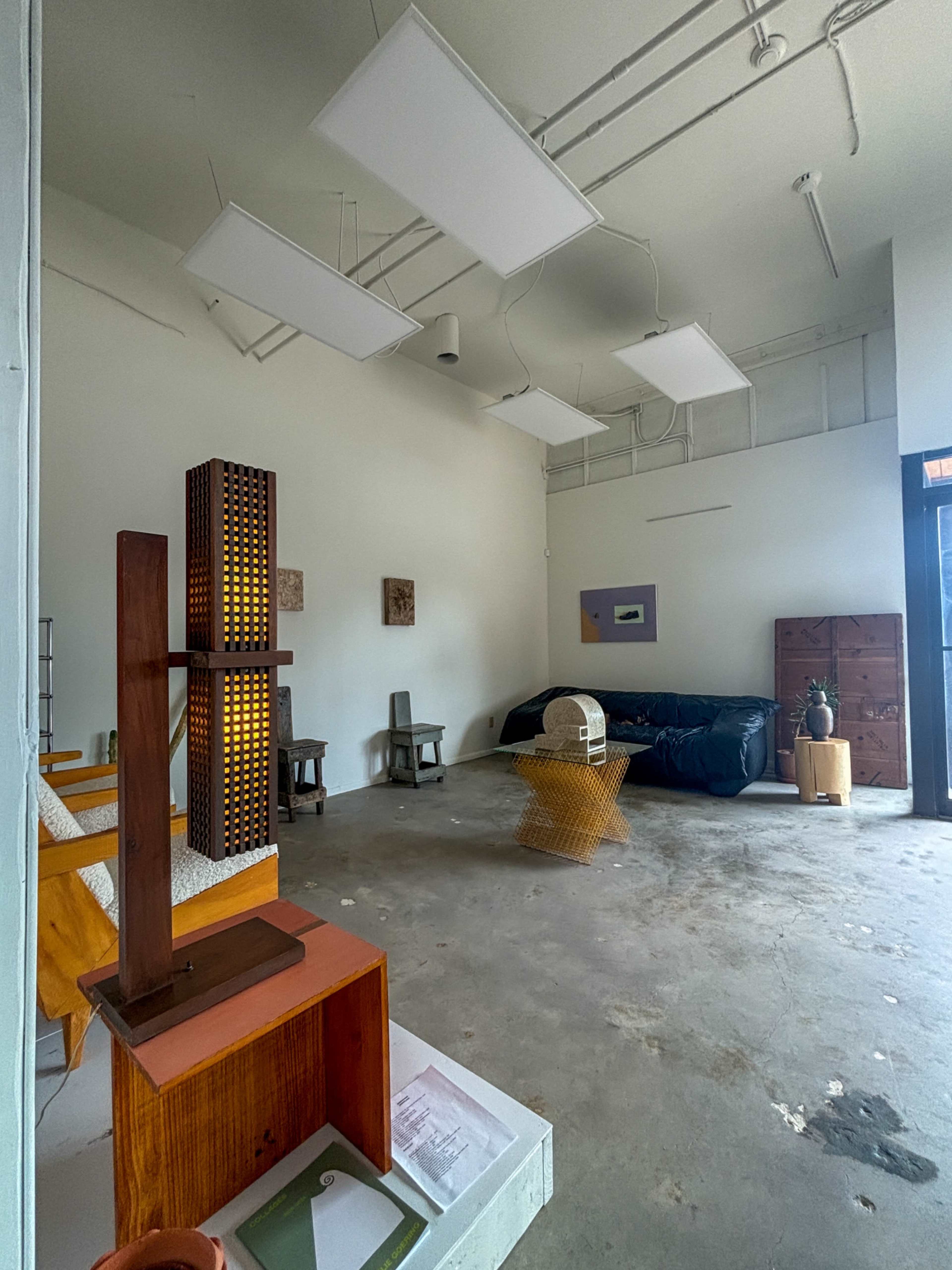 The image shows a minimalistic interior space featuring various furniture pieces, a large black sofa, and abstract art on the walls.