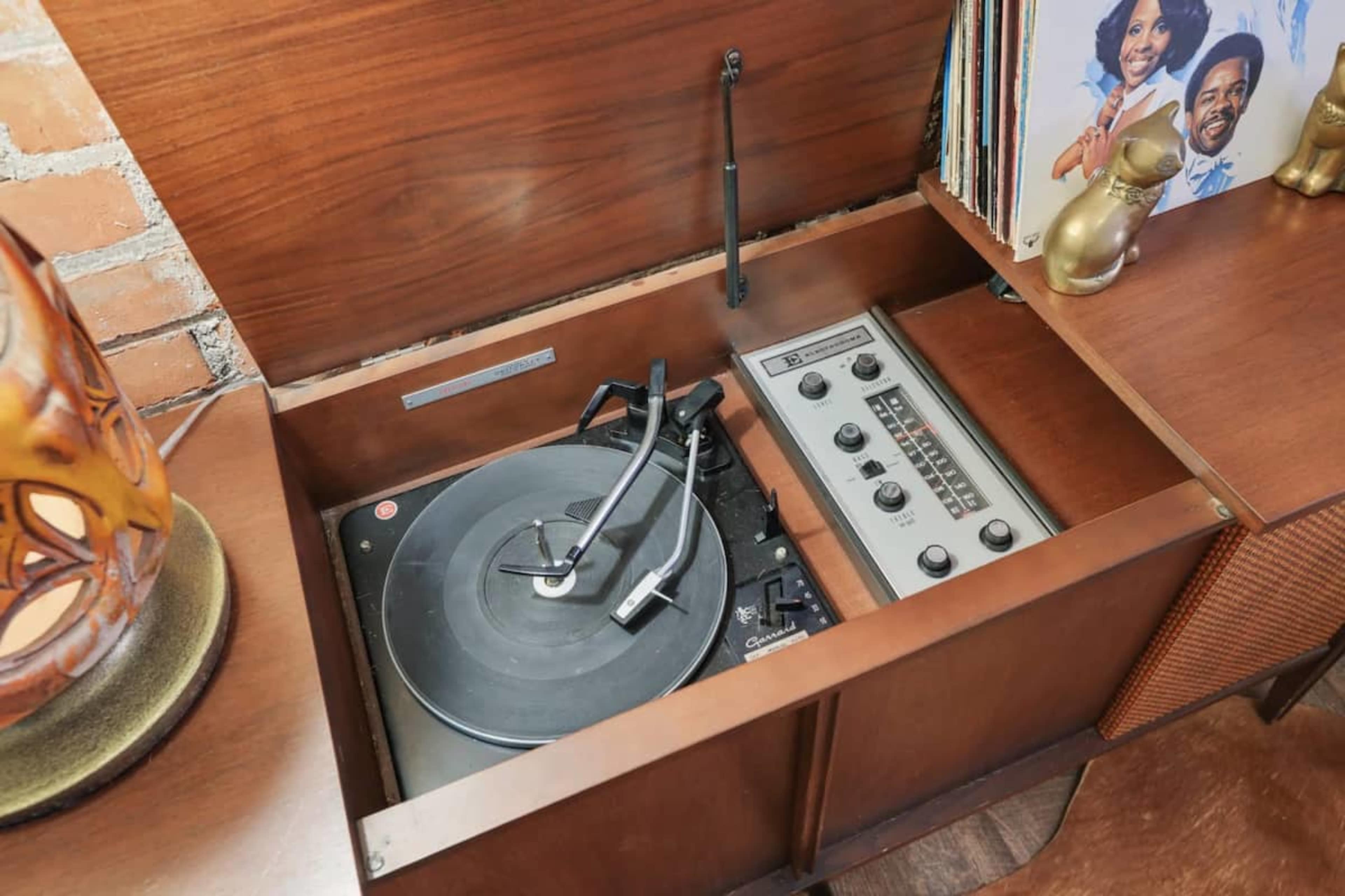 A wooden record player console with a turntable and a control panel, alongside vinyl records displayed in an adjacent section.