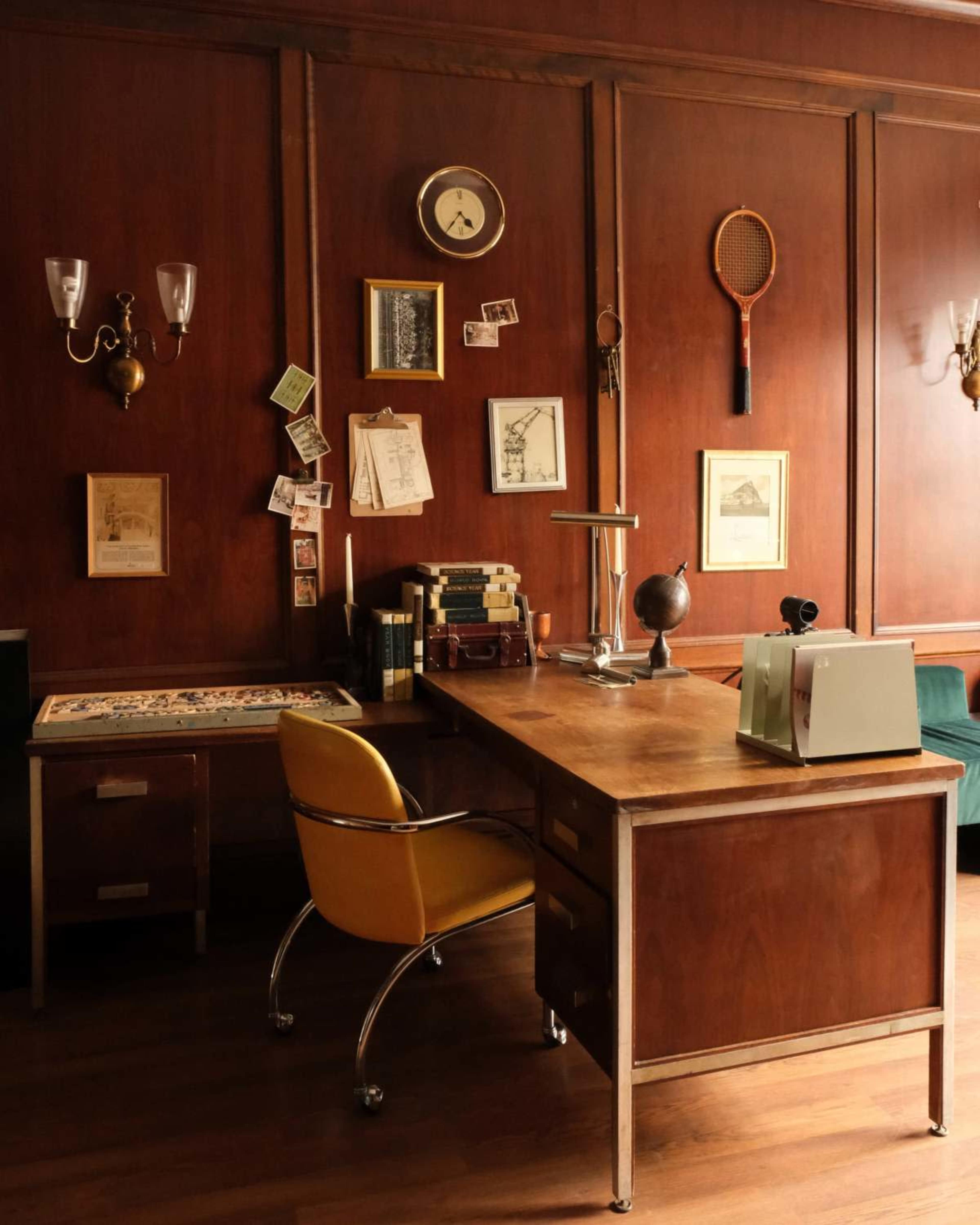 The image depicts a wooden office with a desk, yellow swivel chair, wall decorations including photographs and a clock, and a vintage tennis racket hanging.