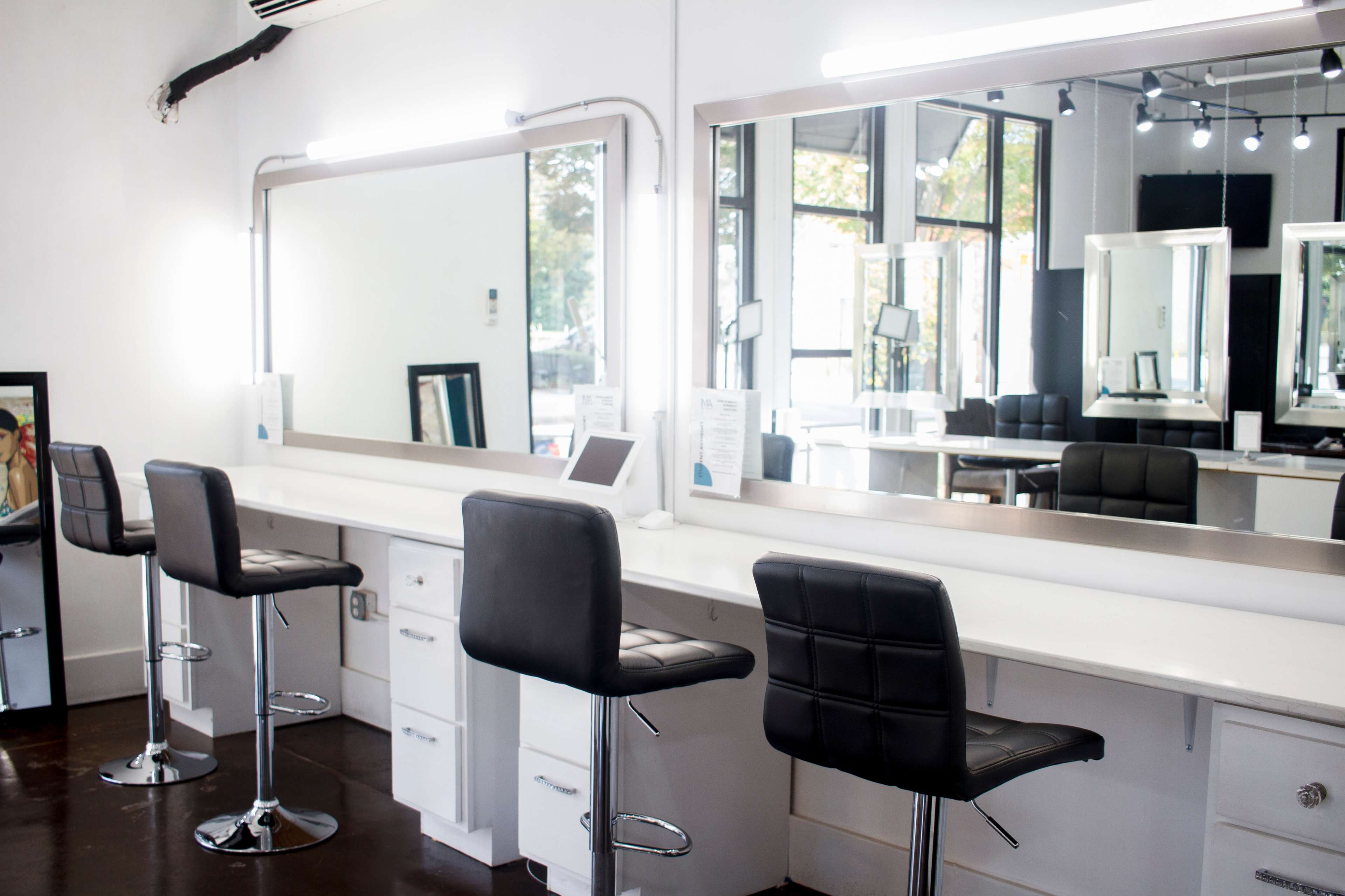 A modern makeup station with two black bar stools in front of large mirrors and a white countertop.