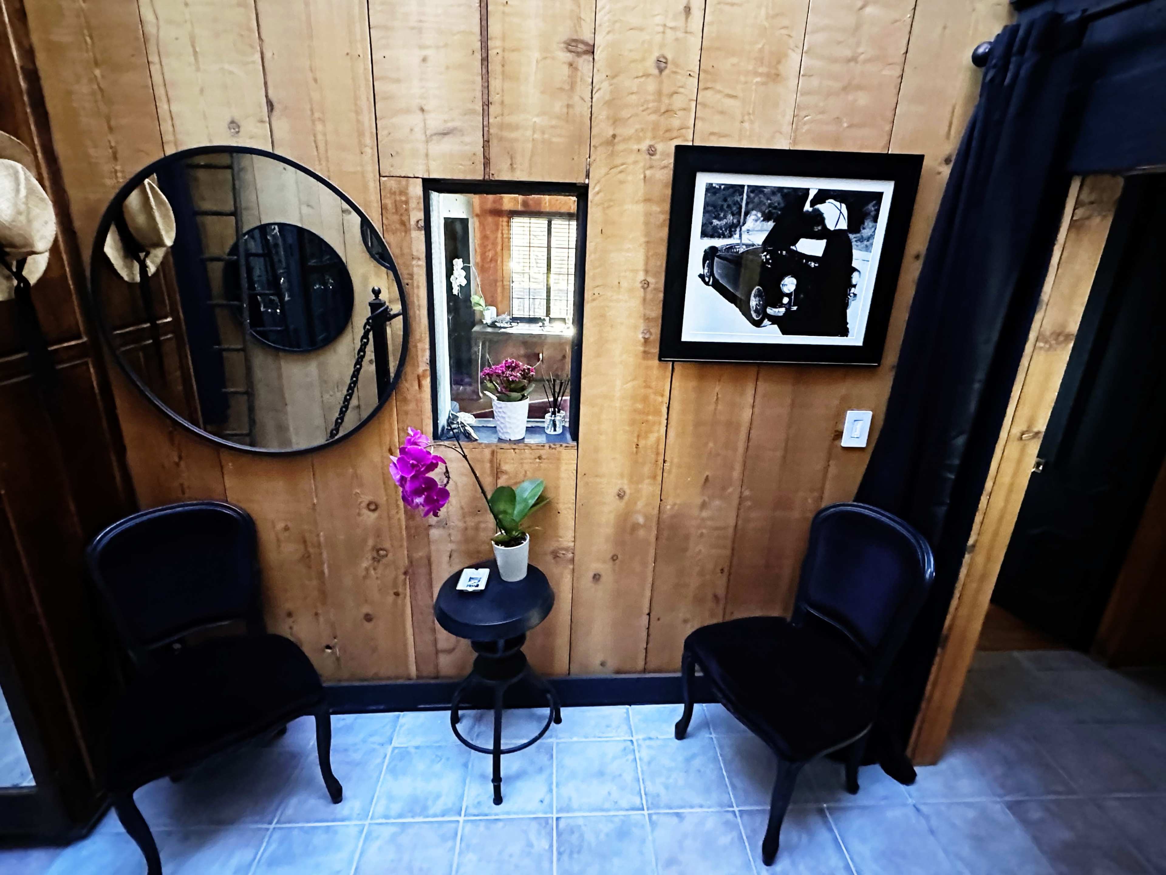 A cozy room with wooden walls, two black chairs, a small round table with a potted orchid, and framed artwork on the walls.