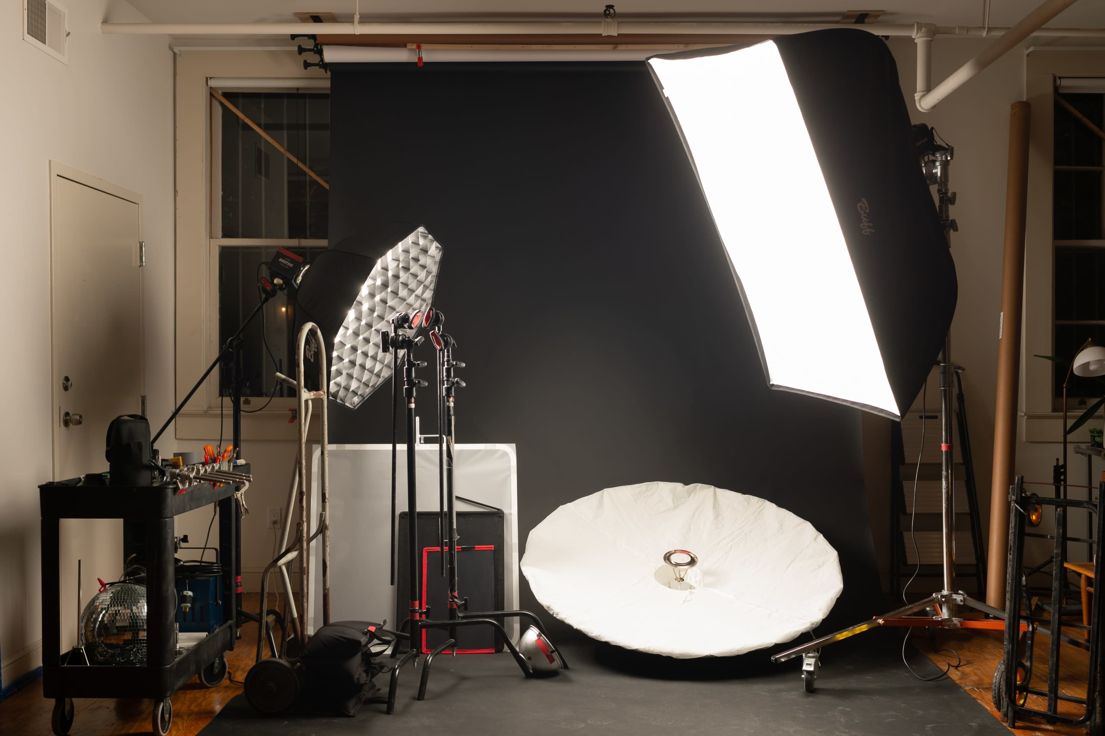 A photography studio setup with various lighting equipment, including softboxes and stands, against a black backdrop.
