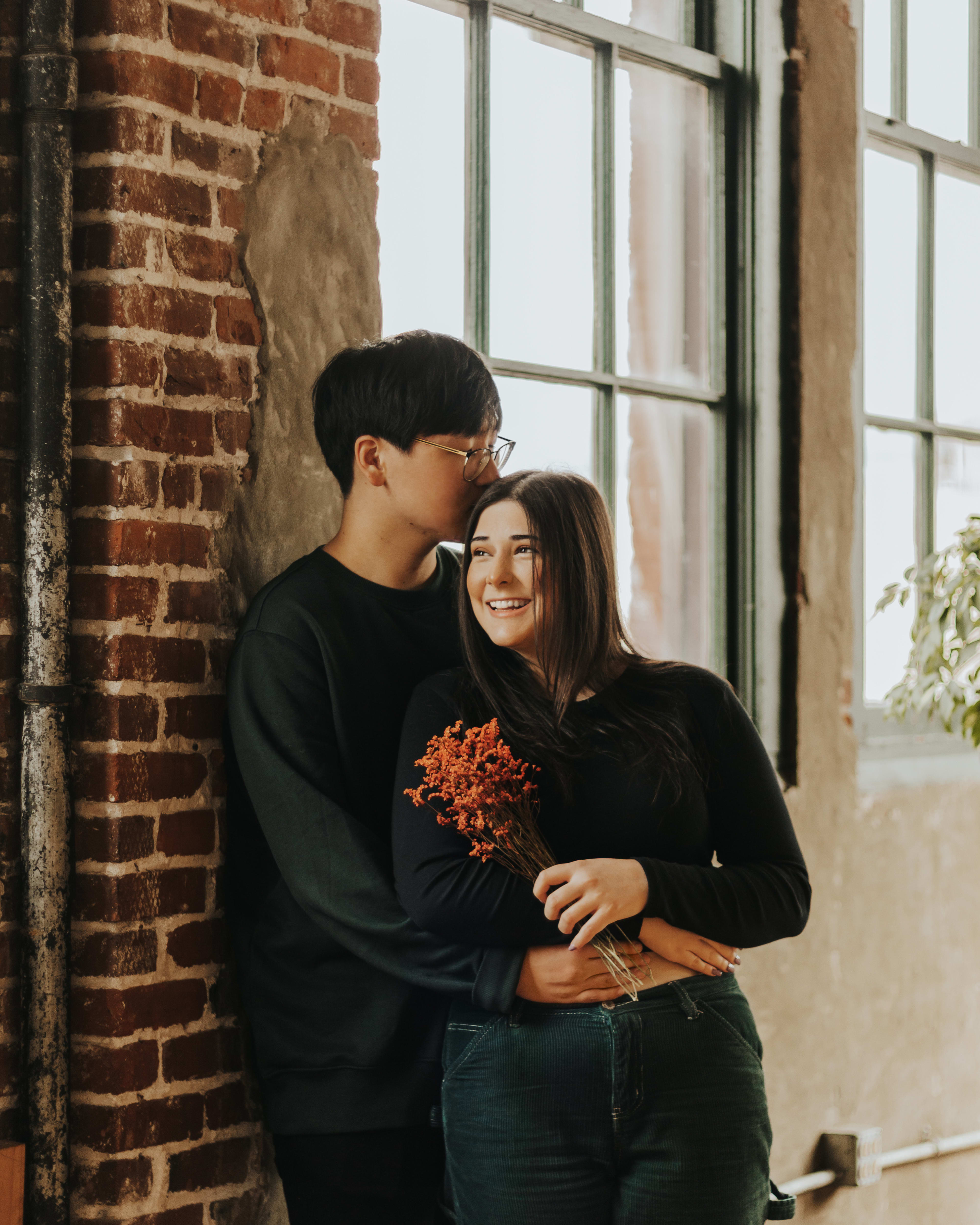 Una pareja posando cerca de una pared de ladrillo durante su sesión de fotos rústica.