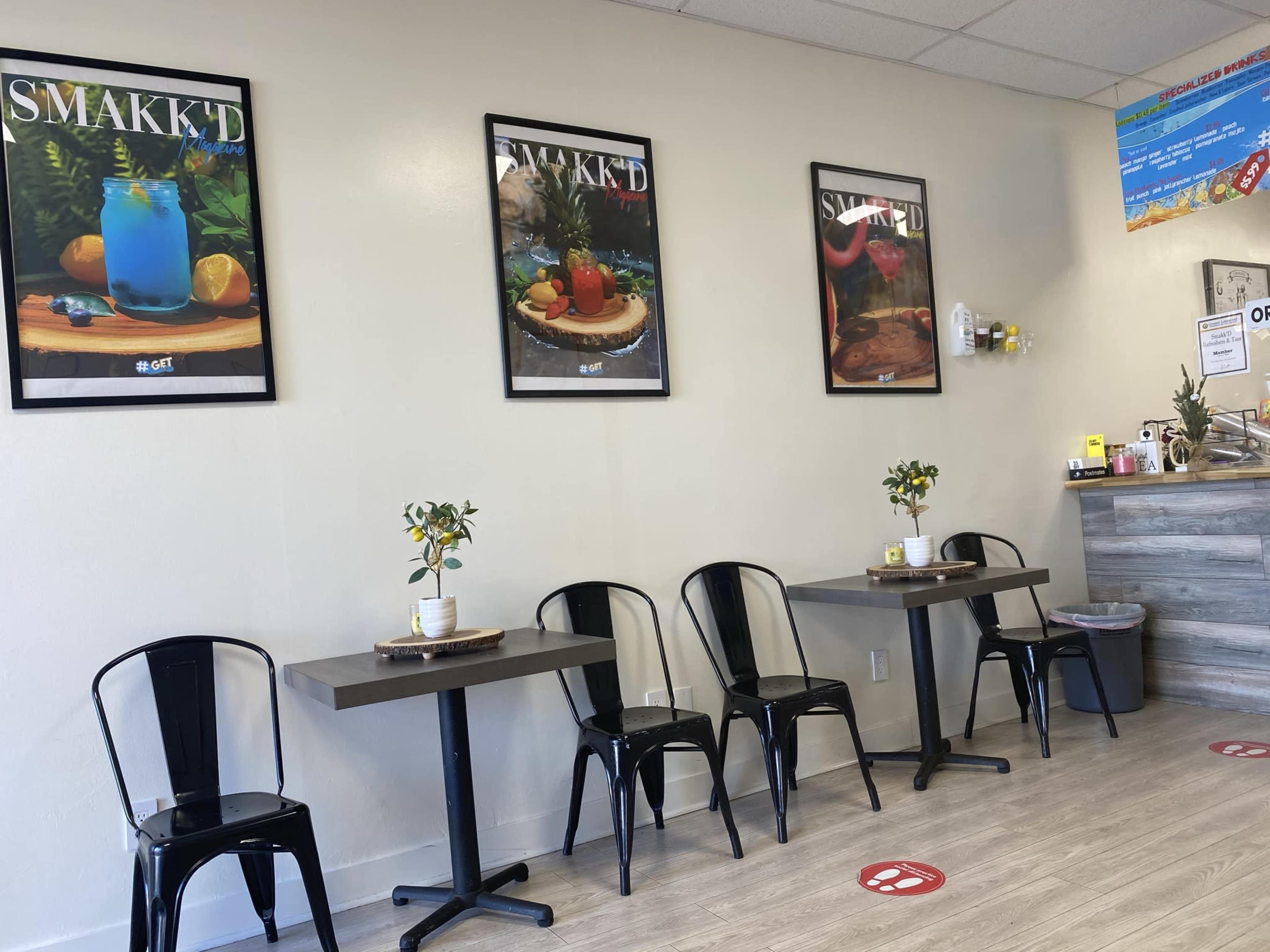 A small cafe interior with three framed posters on the wall, black metal chairs, and wooden tables.