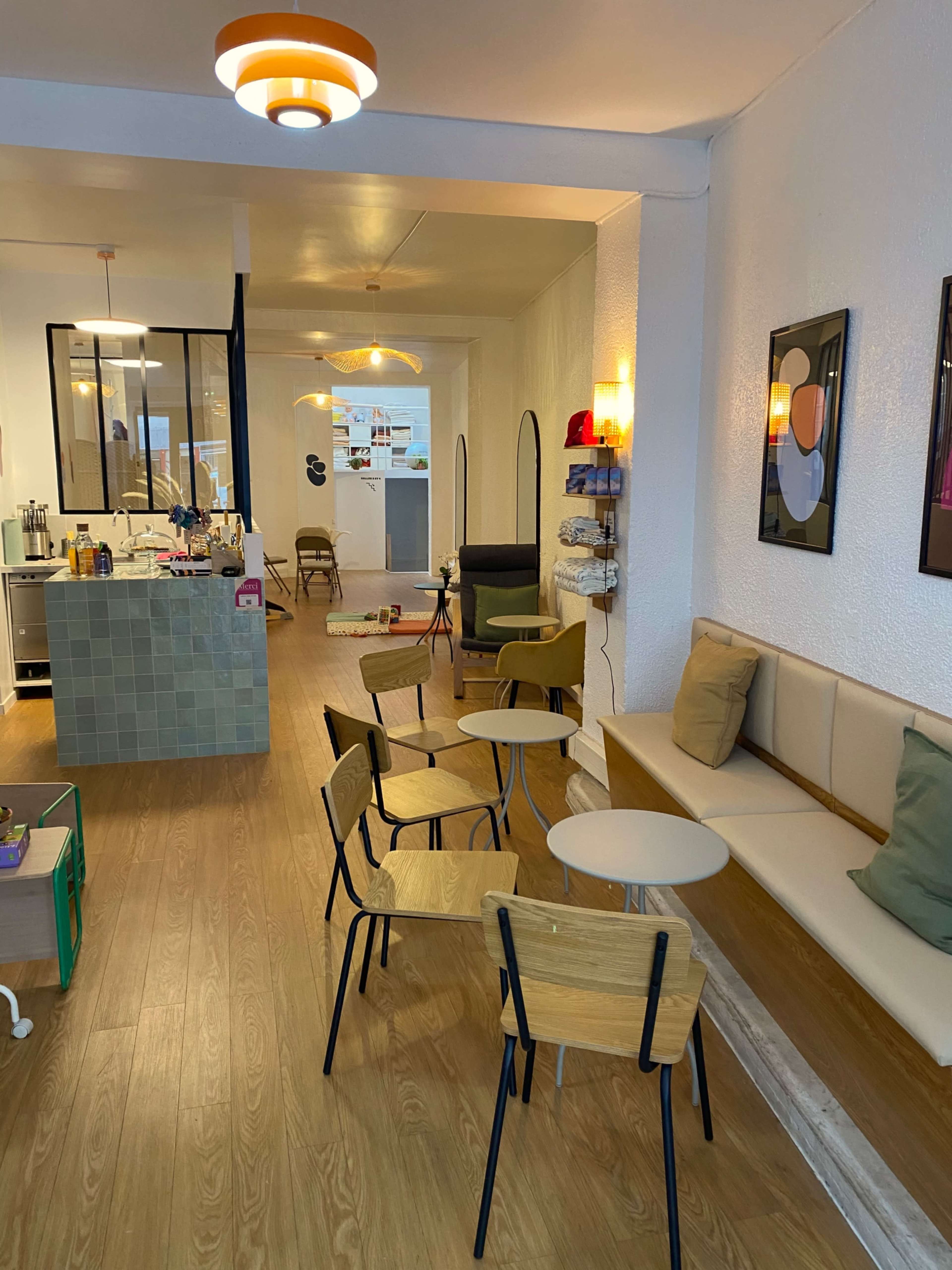The image shows a modern café interior with wooden flooring, a seating area featuring several chairs and tables, and a counter in the background.