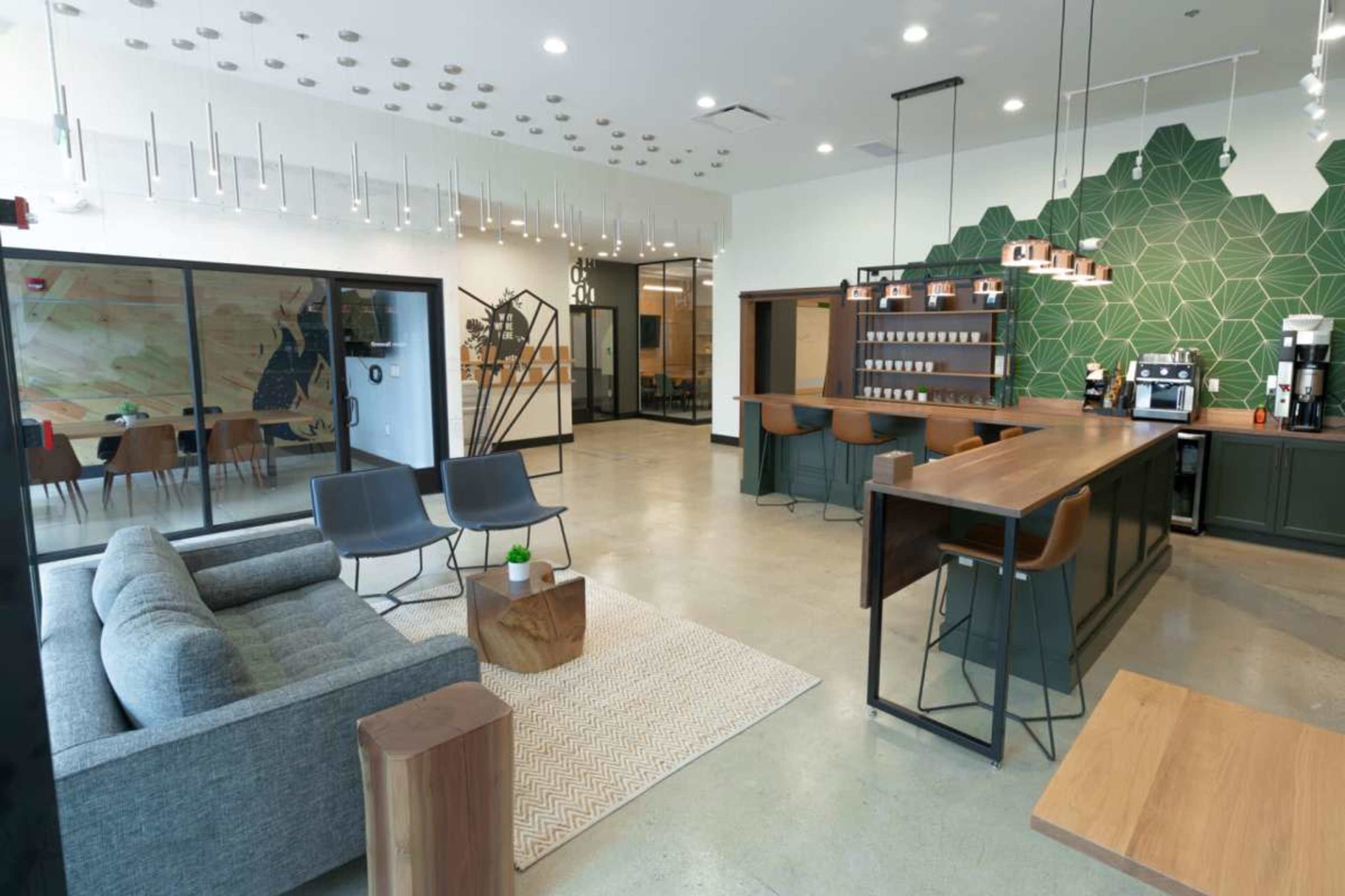 A modern cafe interior features a sleek bar area, cozy seating with gray sofas, and a green geometric accent wall.