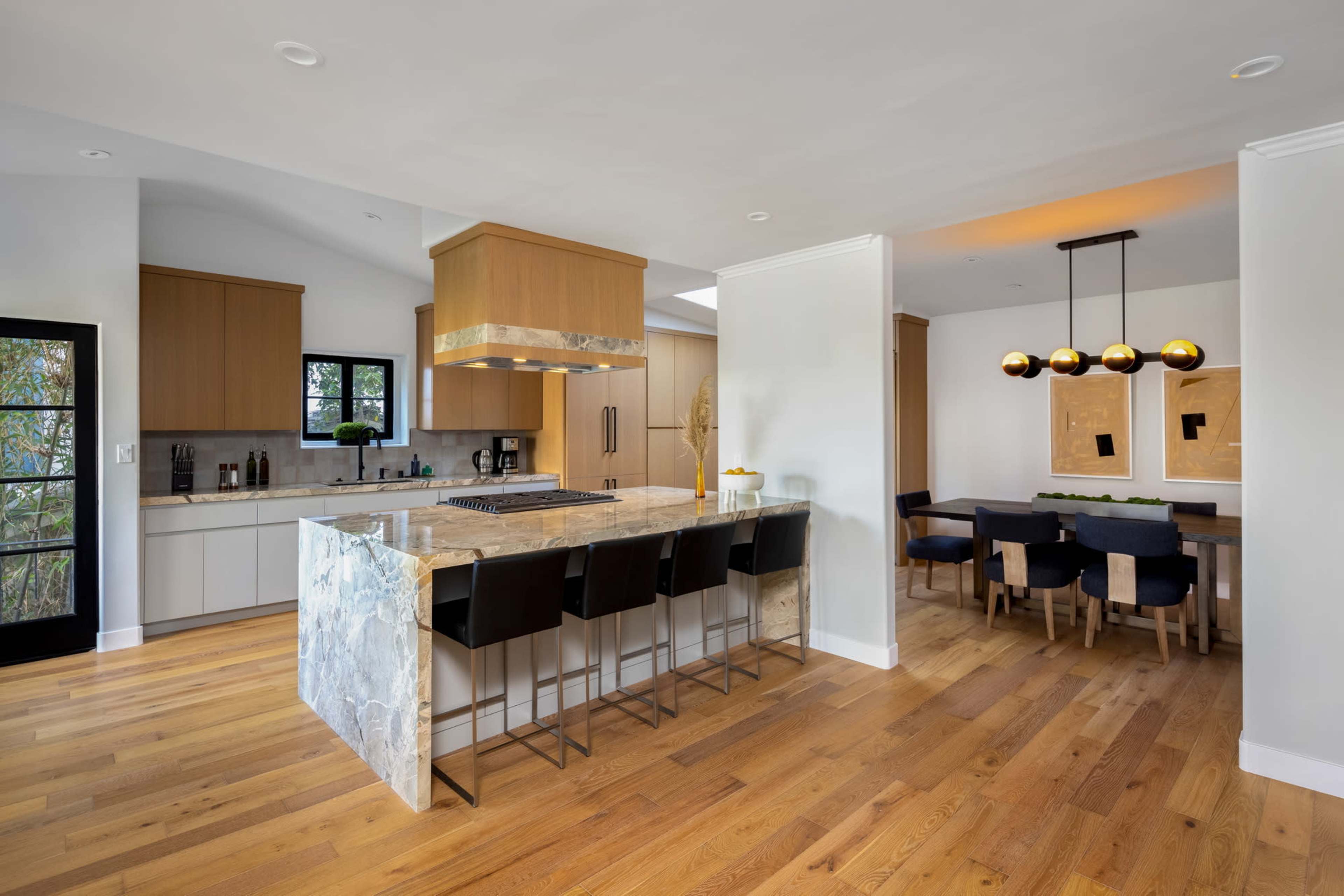 A modern kitchen features a central island with bar stools, adjacent to a dining area with a table and chairs.