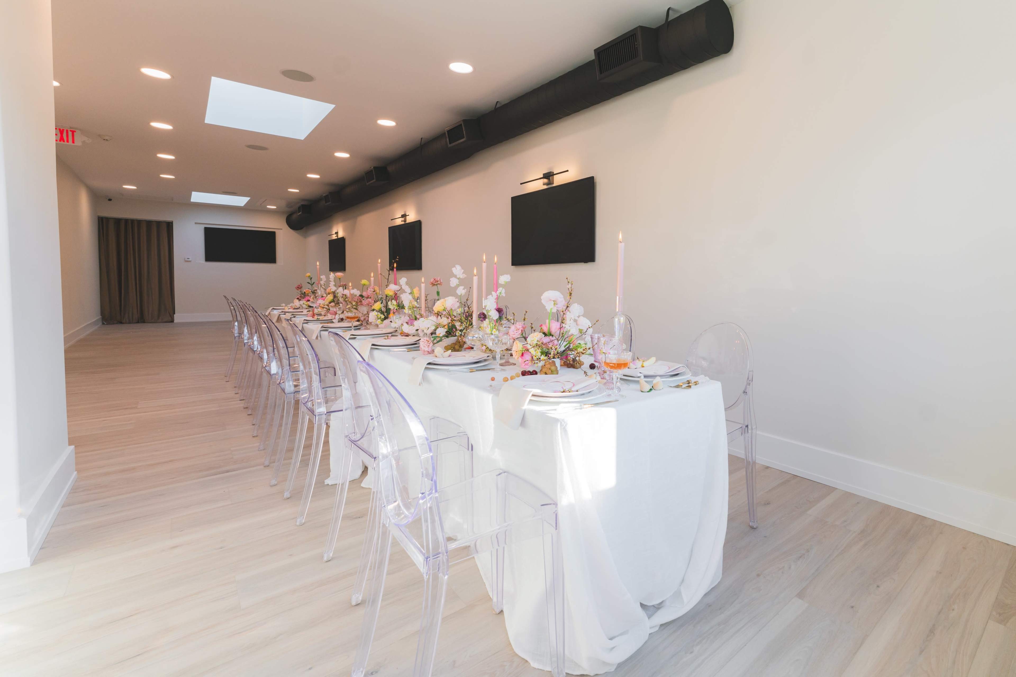 A long dining table is elegantly set with floral centerpieces and candles in a bright, modern room.