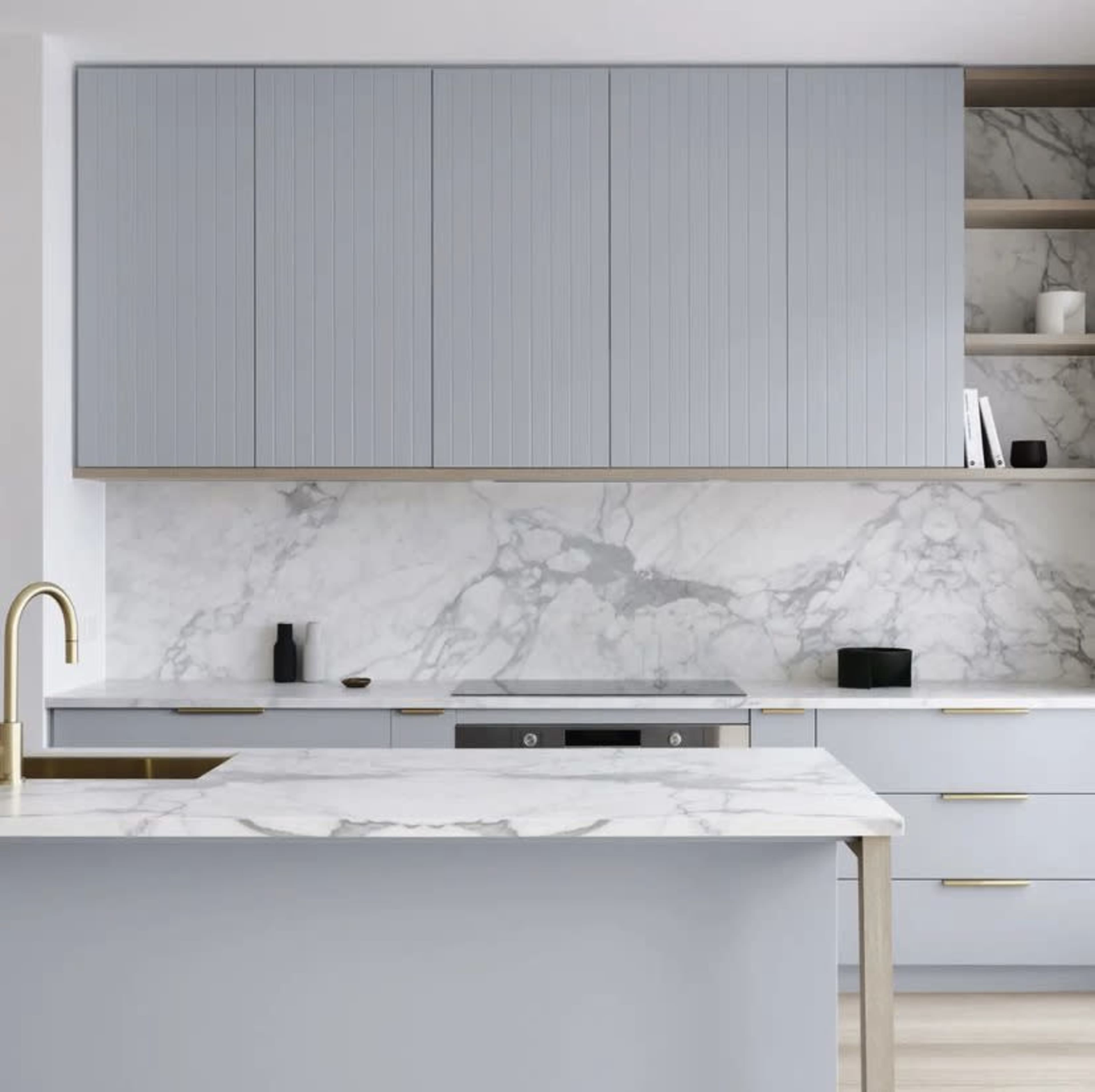 A modern kitchen with light blue cabinetry, a marble backsplash, and a white marble countertop.