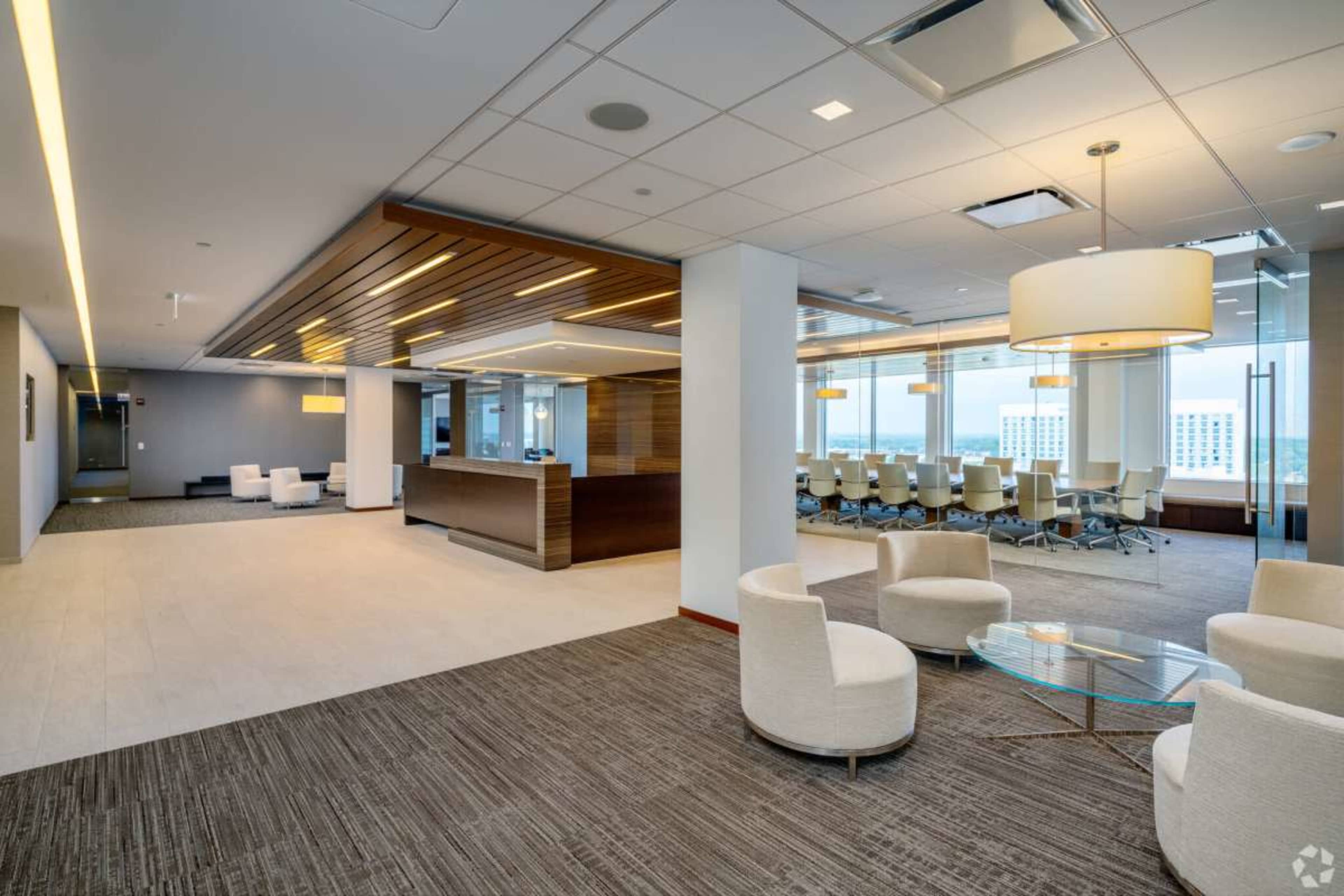 The image shows a modern office space featuring a reception area with a desk, a seating arrangement, and a conference room in the background with large windows.