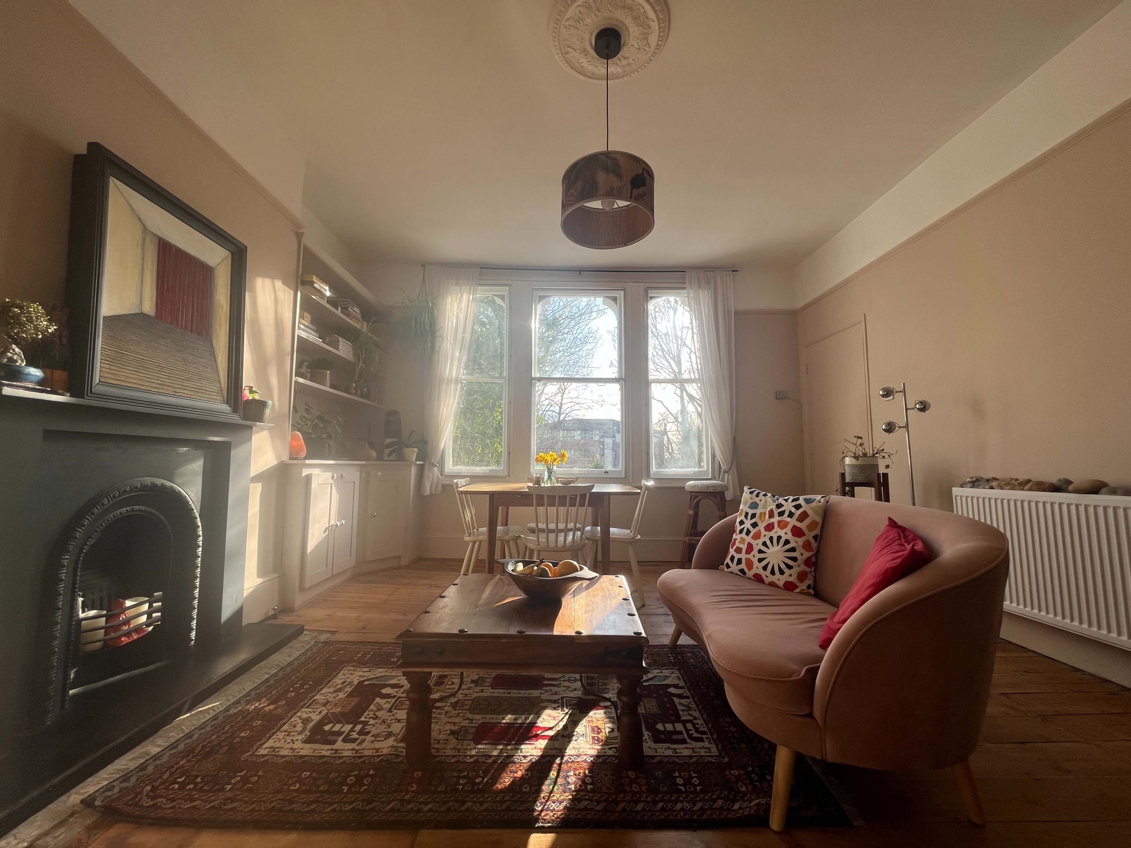 A cozy living room features a sofa, a wooden coffee table, and large windows allowing natural light to stream in.