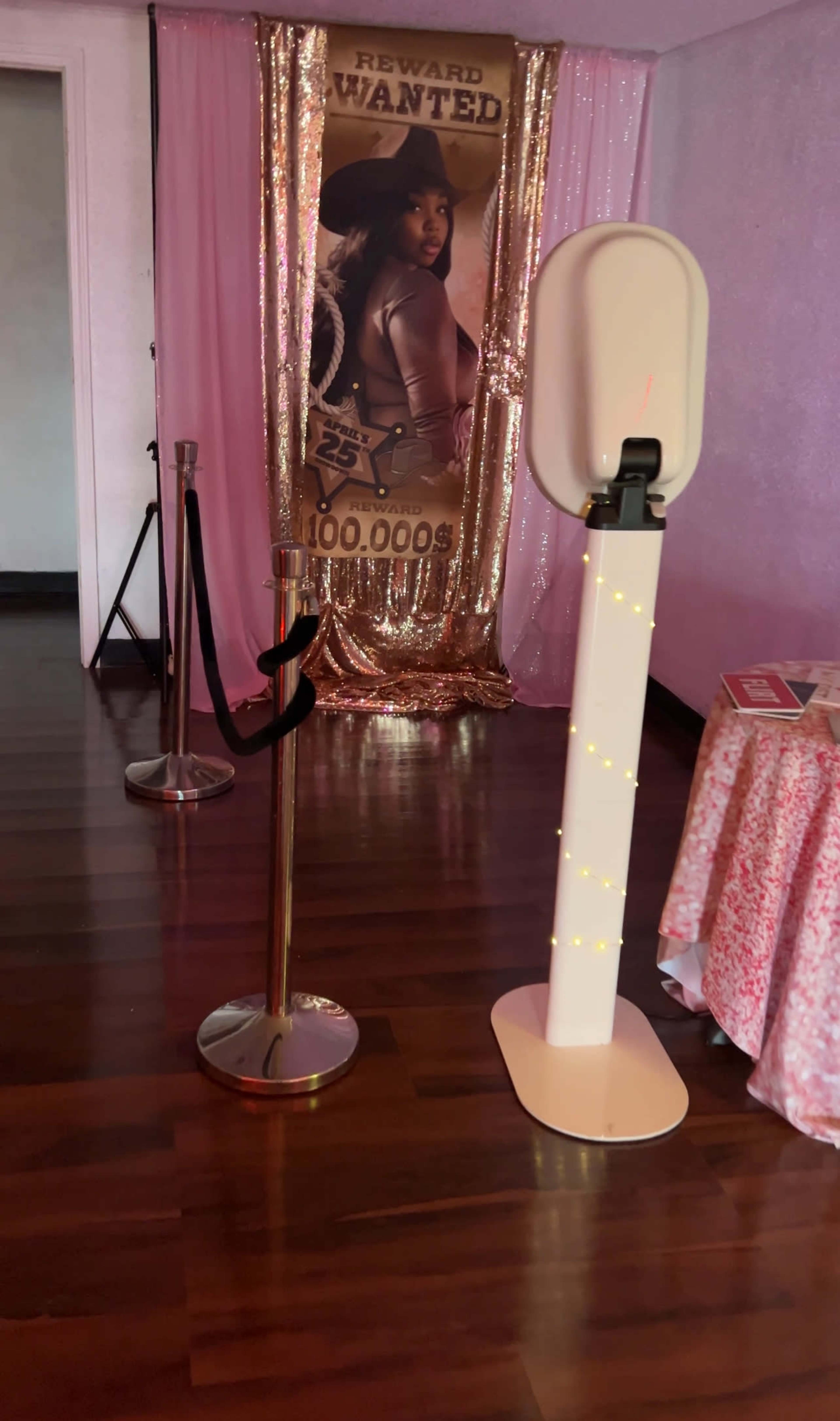 A photo booth set up with a golden backdrop and a "Wanted" poster, along with a queue line barrier and a decorated table nearby.