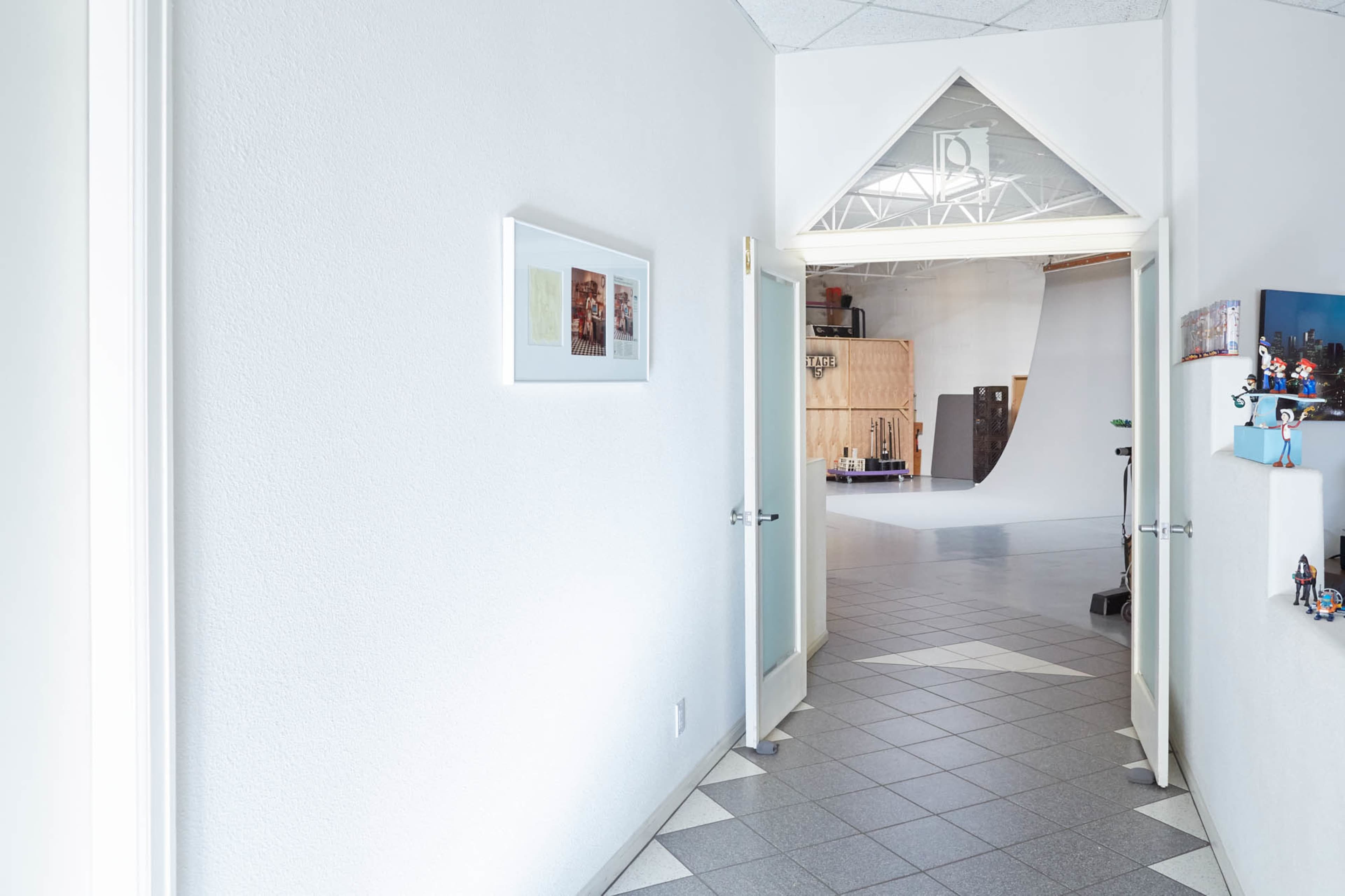 A hallway with white walls leads to an open studio space featuring a curved backdrop and wooden panels.