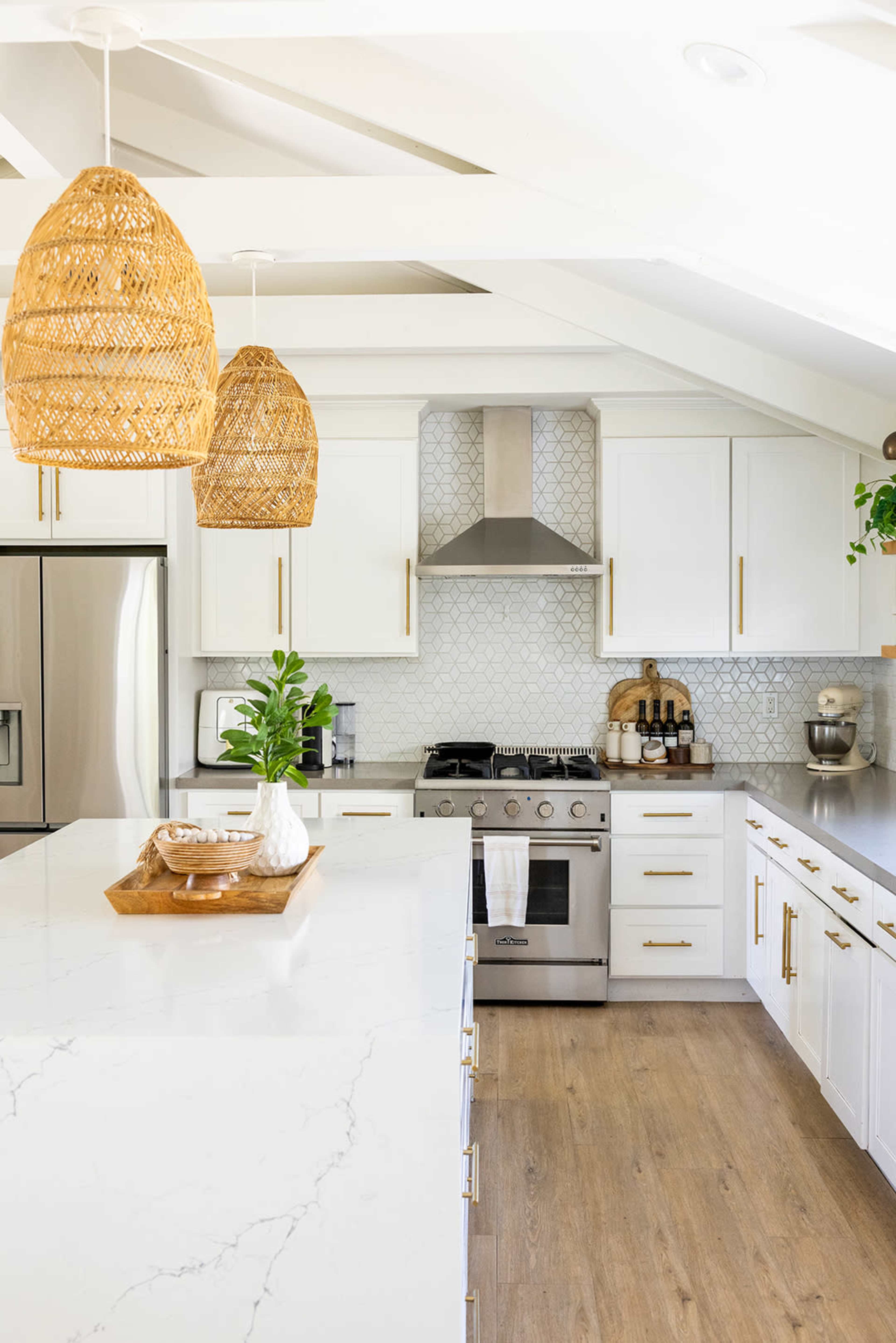 The image depicts a modern kitchen featuring white cabinets, a marble countertop, a stainless steel stove, and rattan pendant lights.