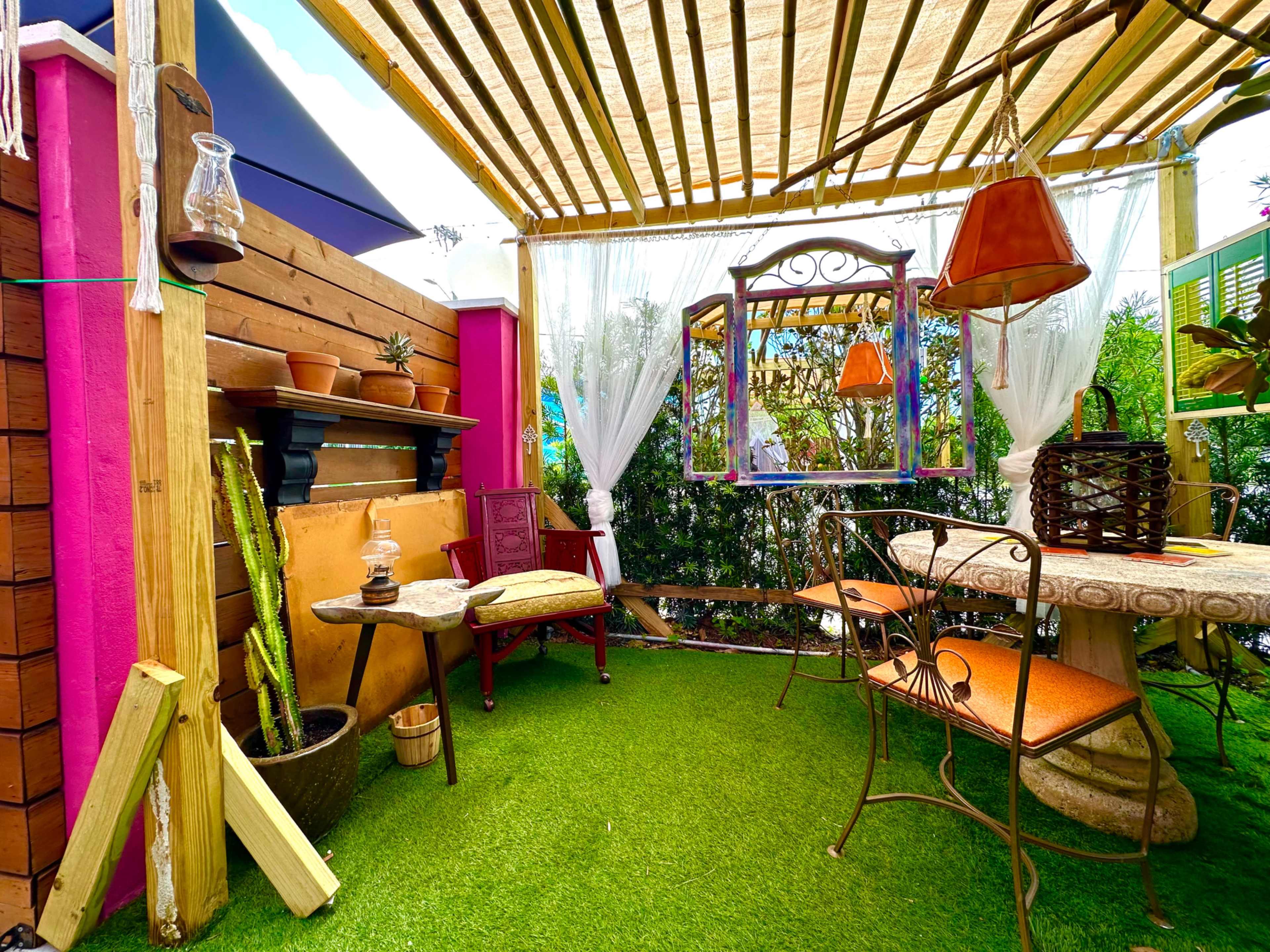A cozy outdoor seating area adorned with potted plants, a decorative mirror, and a rustic table under a shaded pergola.