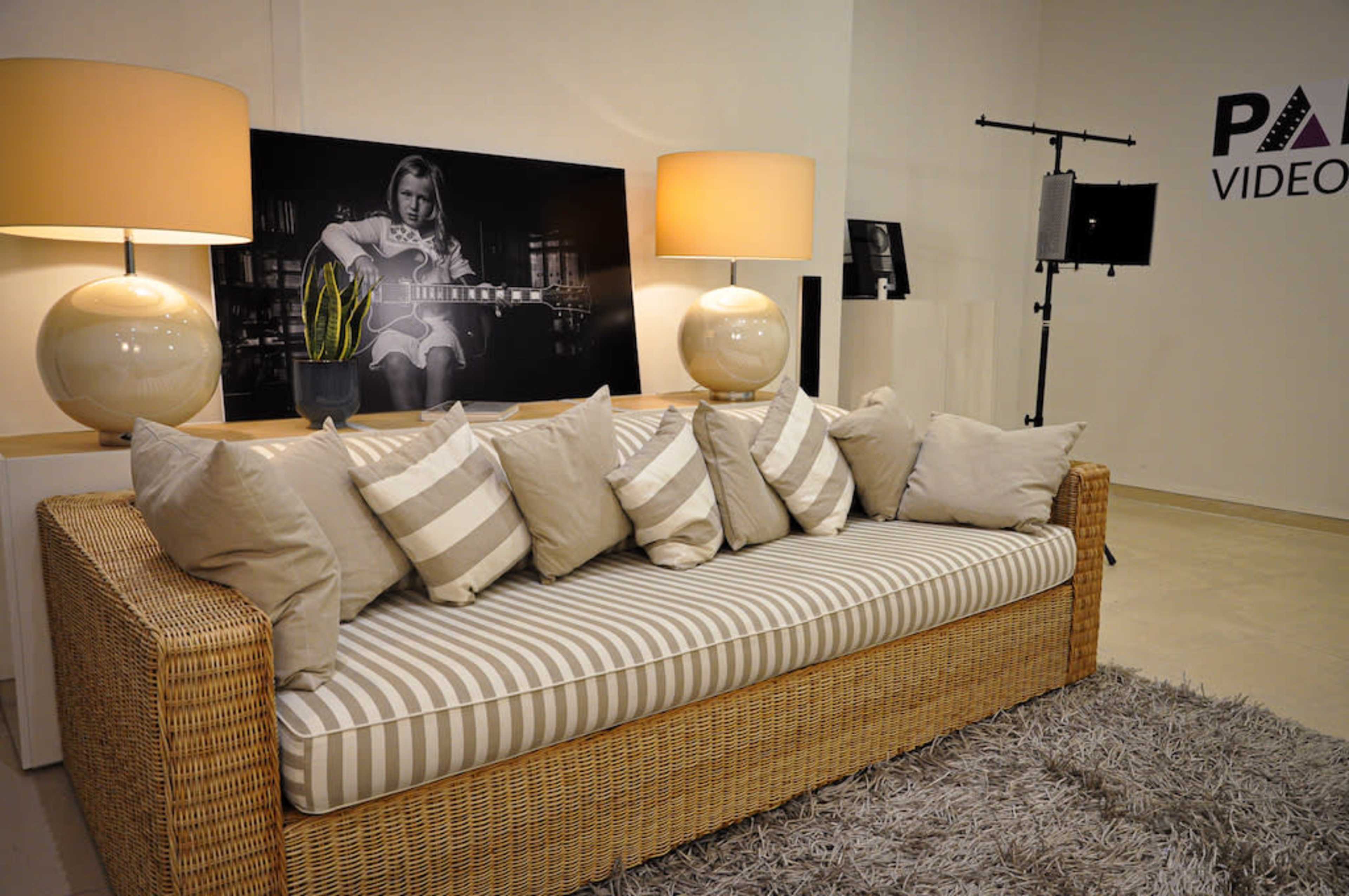 A wicker sofa with striped cushions is positioned in a modern room featuring two lamps and a large black-and-white photo of a person playing guitar on the wall.