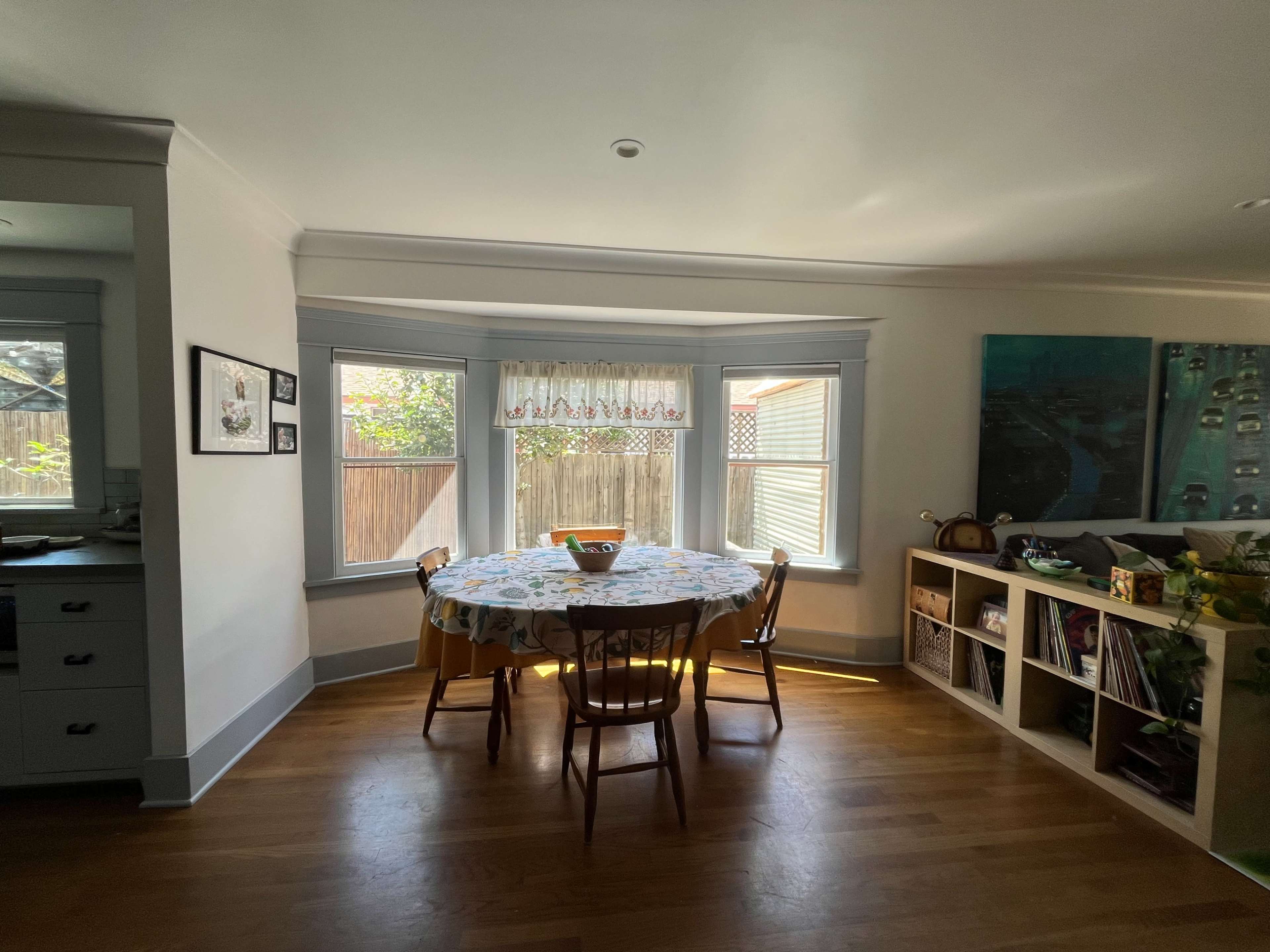 A round table with four chairs sits in a brightly lit dining area near large windows.