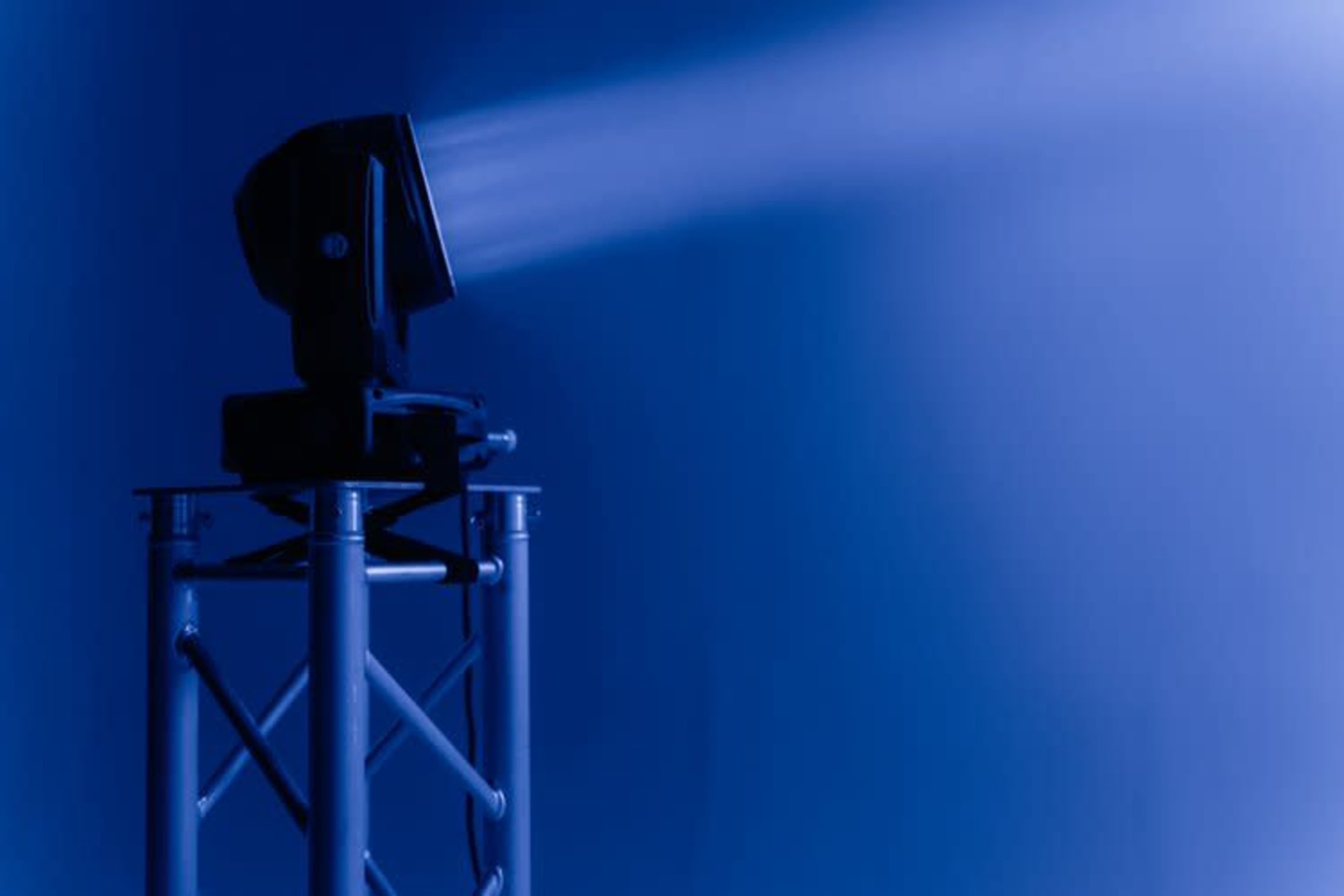 A stage light projects a beam of light against a blue backdrop.