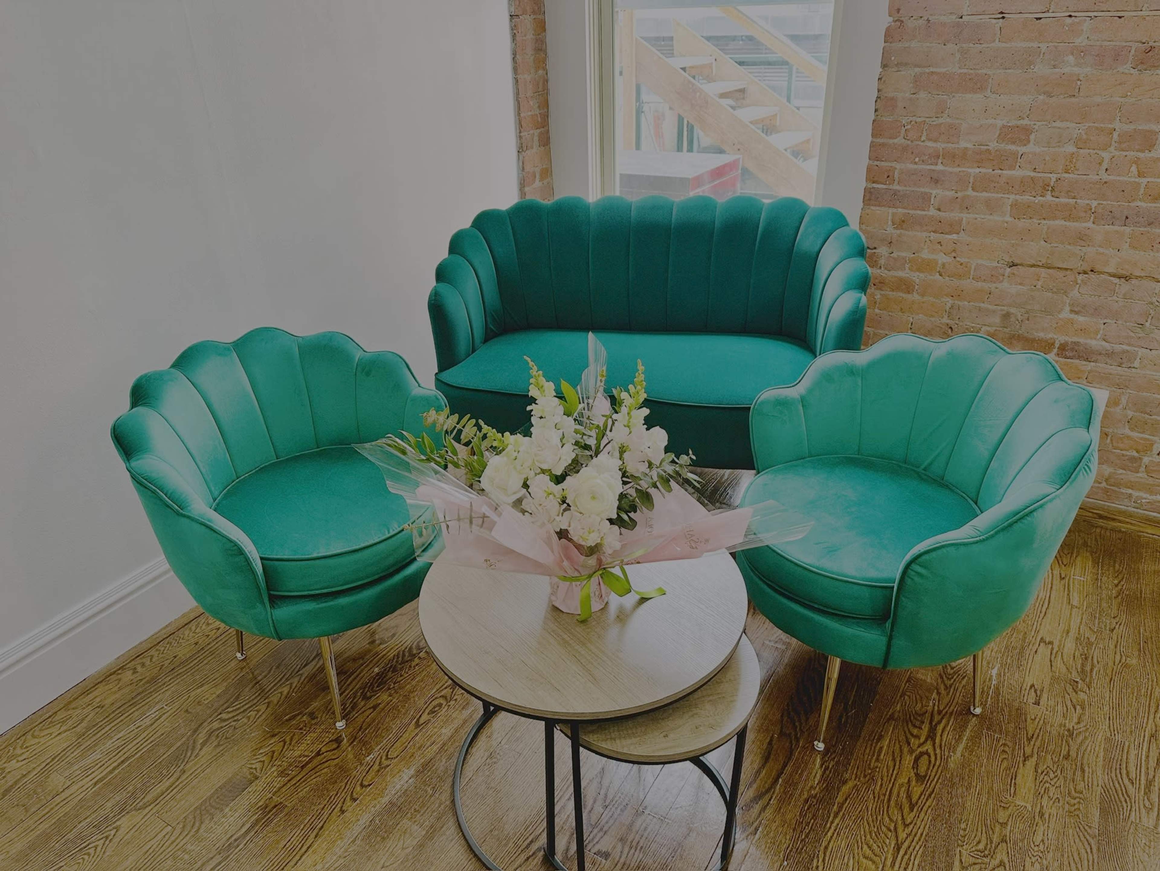The scene features a stylish seating area with a green scalloped back sofa and two matching chairs surrounding a round wooden coffee table adorned with a floral arrangement.