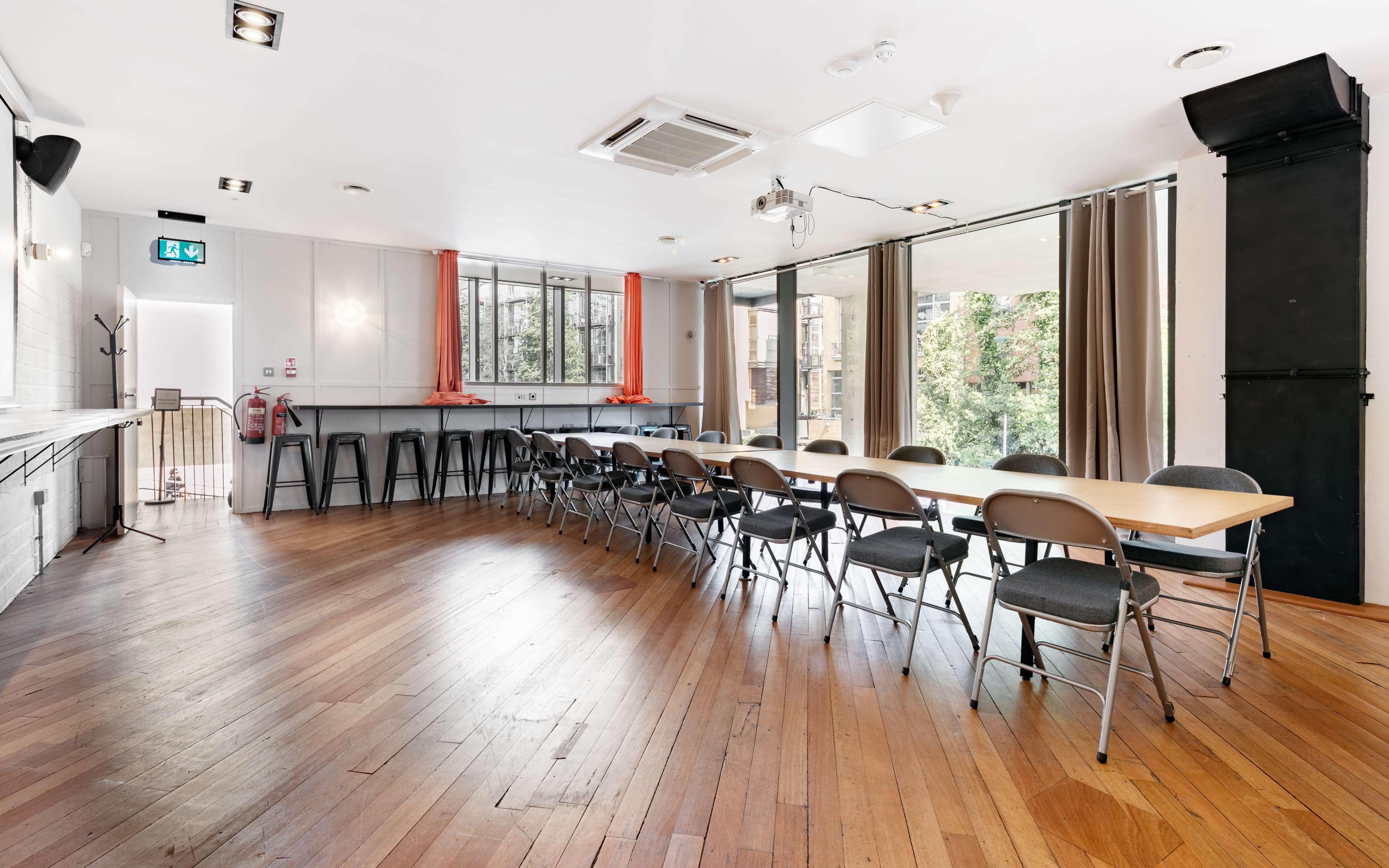 A spacious meeting room features a long table with chairs arranged facing large windows that overlook greenery.