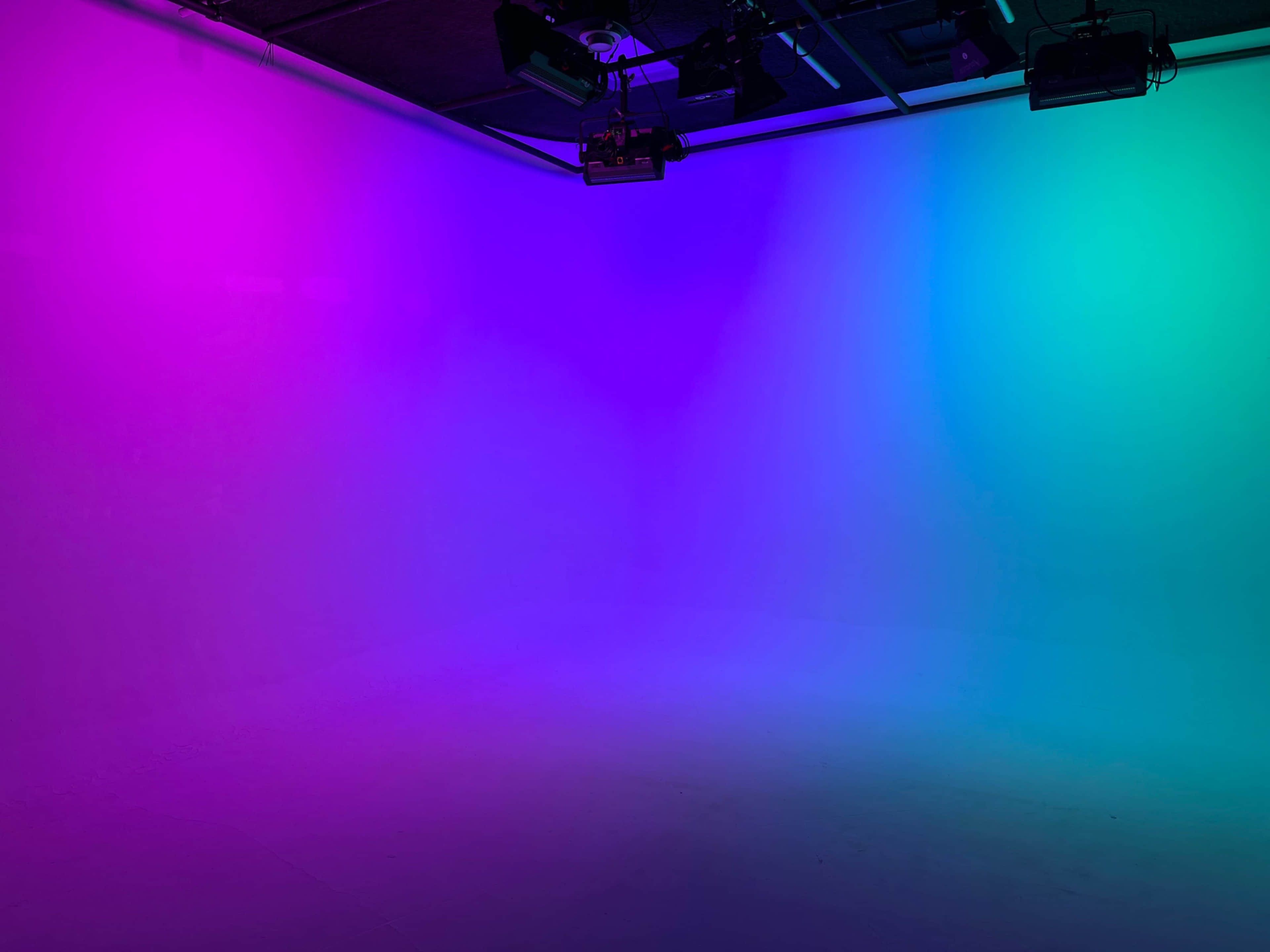The image shows an empty studio space illuminated with a gradient of pink and blue lighting.