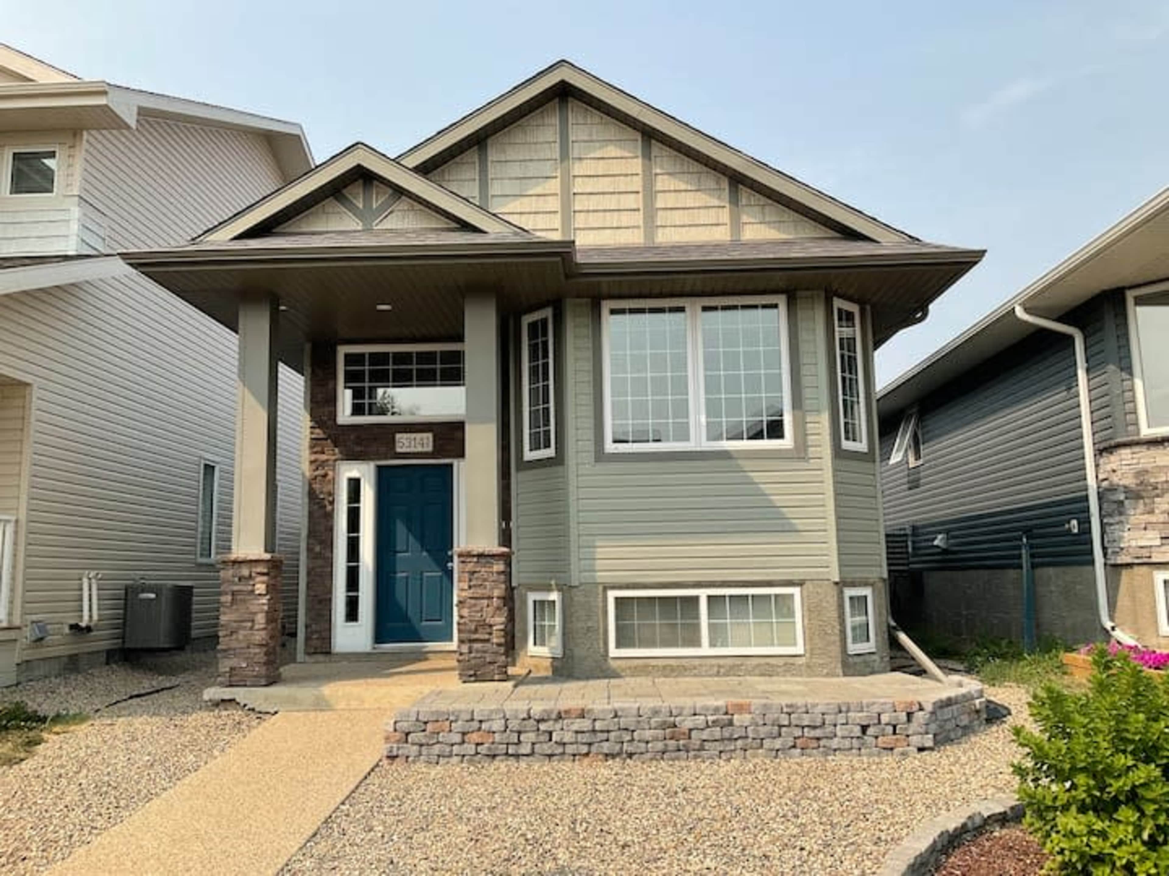 The image shows a modern house with a distinctive front porch, large windows, and stone accents in a residential neighborhood.