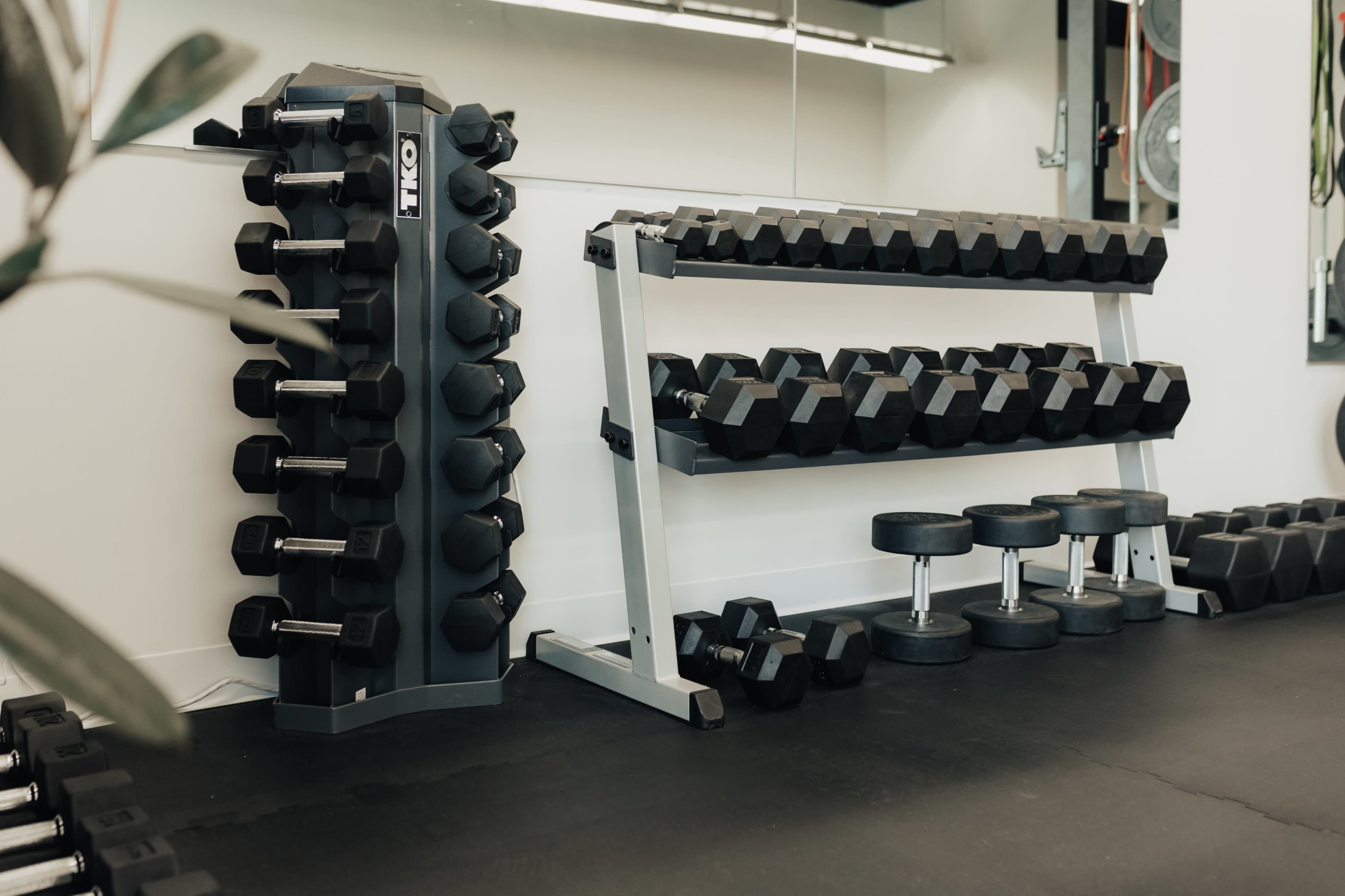 A fitness room with a rack of dumbbells, a weight stand, and a set of flat benches on a black floor.