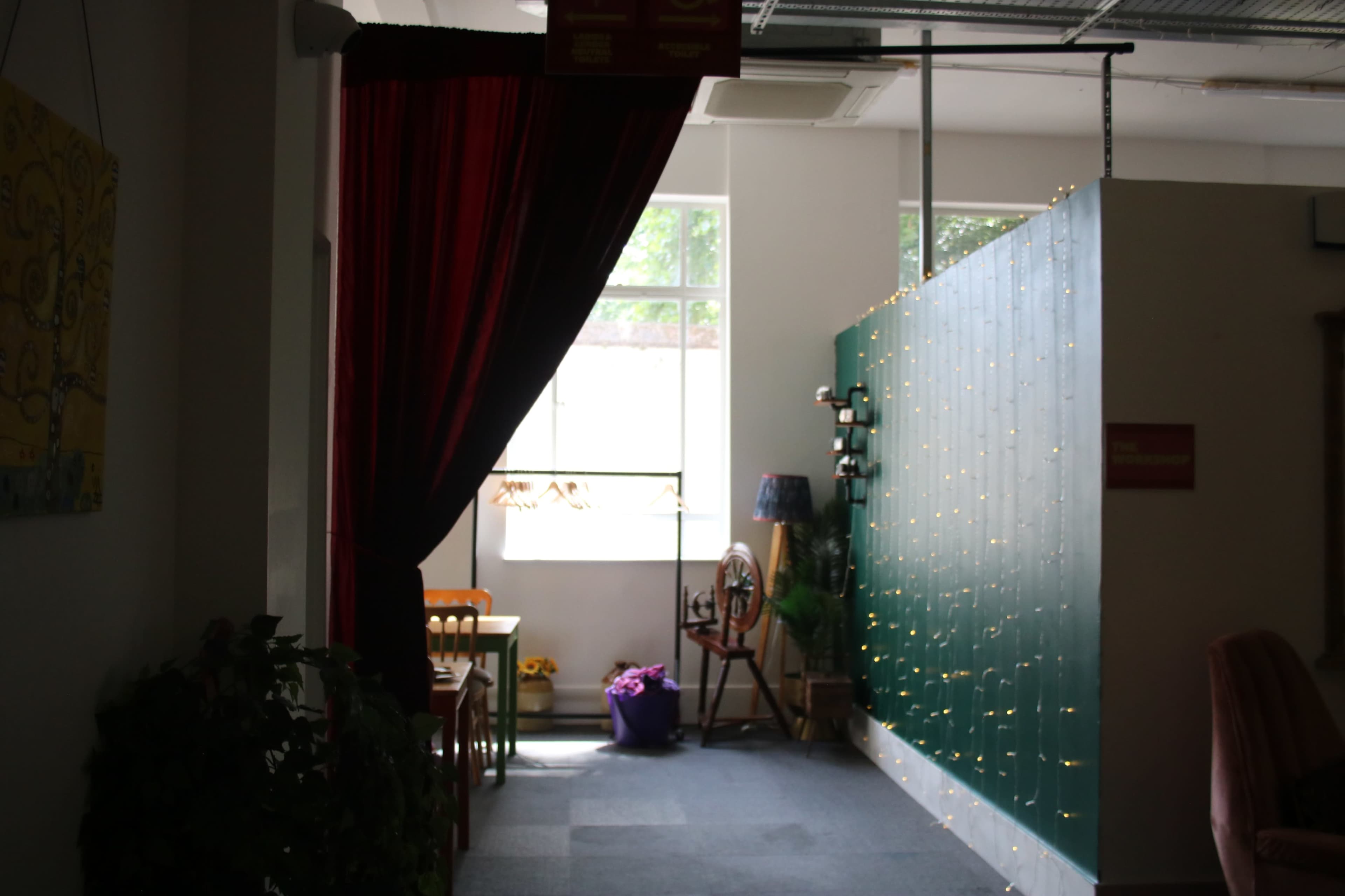 The image shows a hallway with a red curtain, a green wall adorned with lights, and a small seating area with chairs and a lamp.